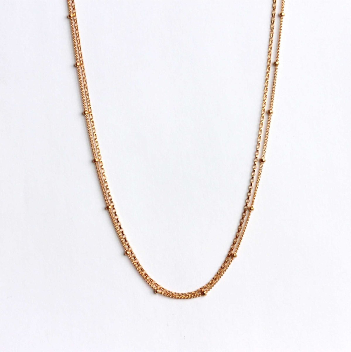 Eine goldene Halskette, bestehend aus einer Erbskette und einer Satellitenkette hängt vor einem weißen Hintergrund.