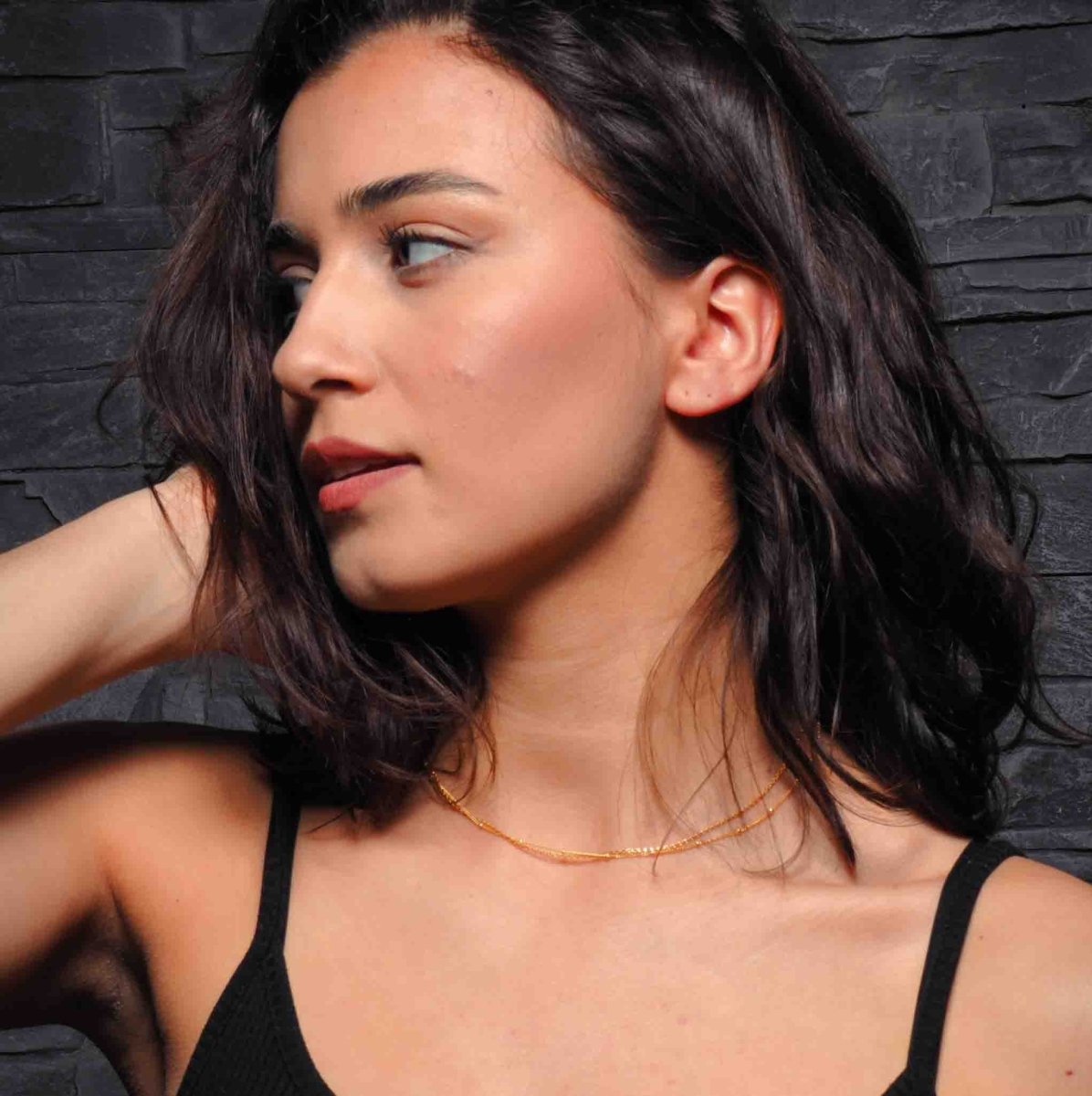 Eine goldene Halskette, bestehend aus einer Satellitenkette und einer Erbskette hängt um den Hals des Models.