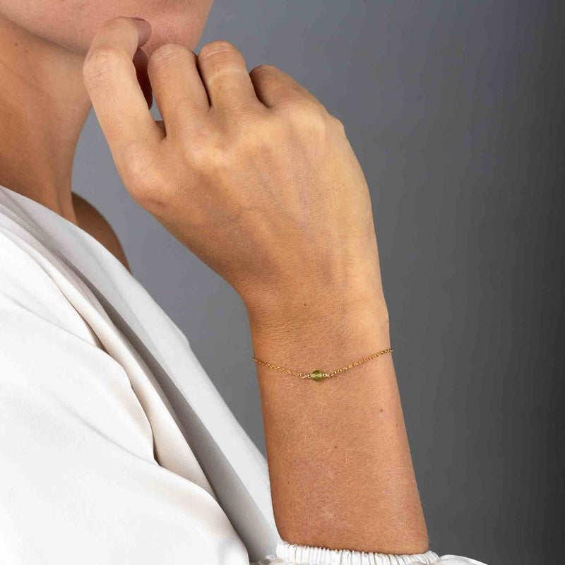 Nahaufnahme eines dünnen, goldenen Armbandes mit einer runden Peridot-Perle in der Mitte am Handgelenk des Models