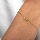 Nahaufnahme eines dünnen, goldenen Armbandes mit einer runden Peridot-Perle in der Mitte am Handgelenk des Models