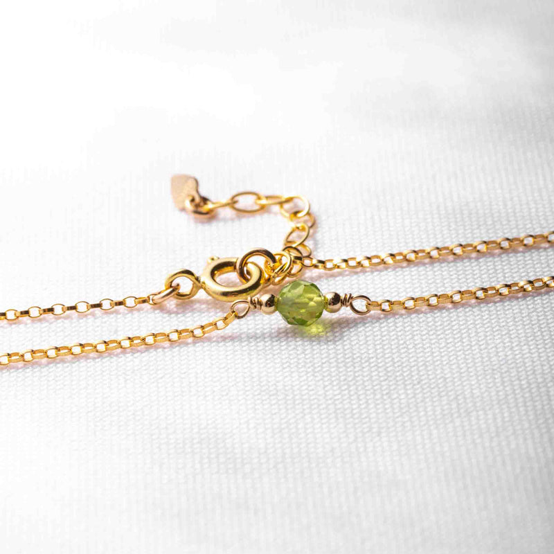 Goldenes Armband mit feiner Kette und einem zentralen, facettierten Peridot-Edelstein, fotografiert auf einem weissen Hintergrund. Produkt von Mayam Berlin