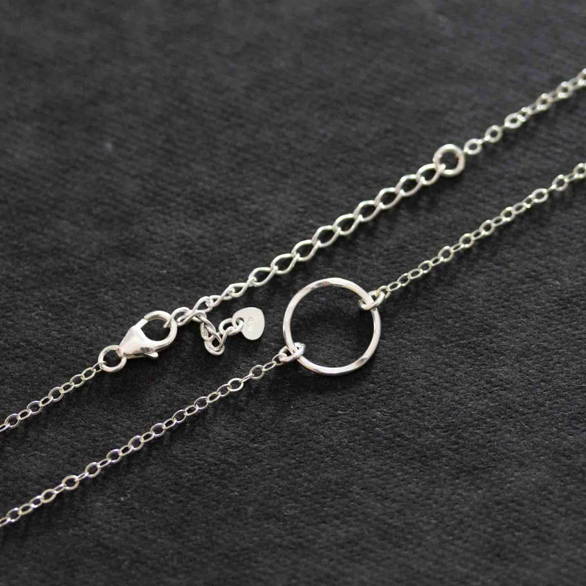 Eine Halskette aus 925 Silber mit einem offenen, gehämmerten Ring als Verbinder auf dunklem Hintergrund.
