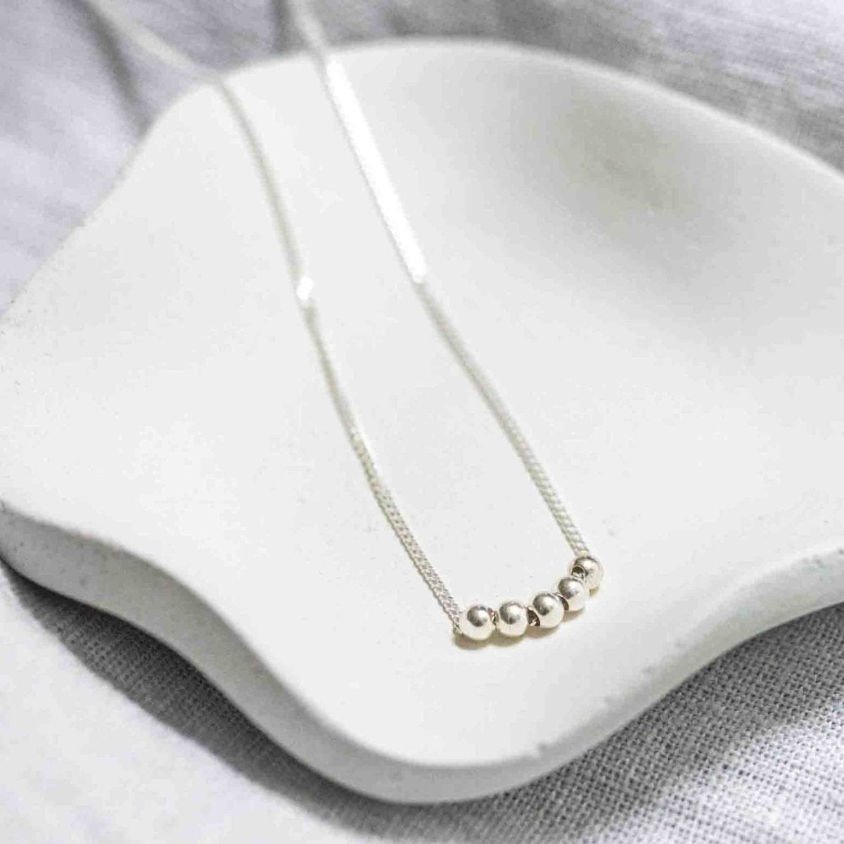 Eine feine 925 Sterlingsilber-Kette mit fünf kleinen silbernen Perlen auf weißem Hintergrund.
