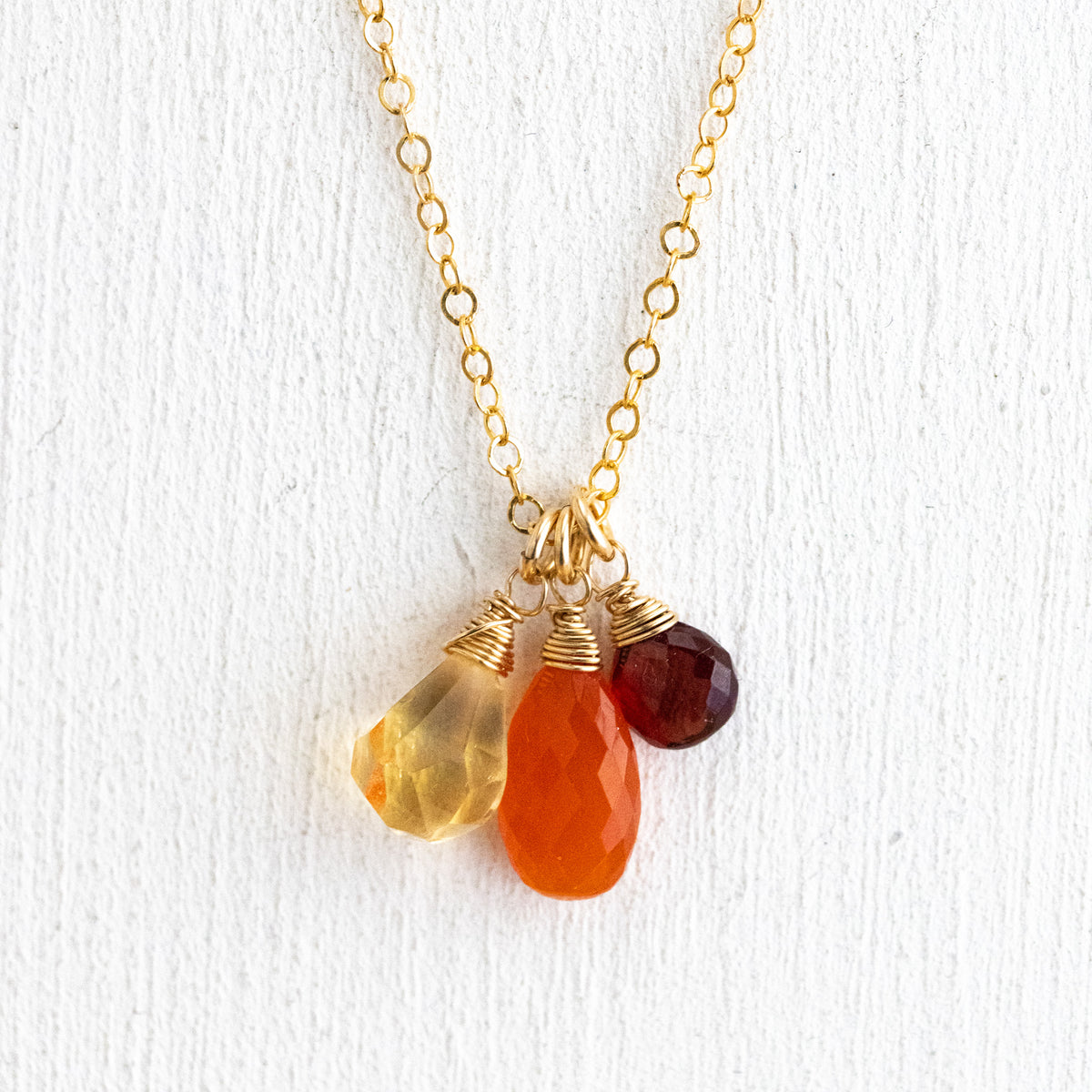 Zierliche Goldkette mit Citrin-, Karneol- und Granat-Anhänger vor weißem Hintergrund gehängt.