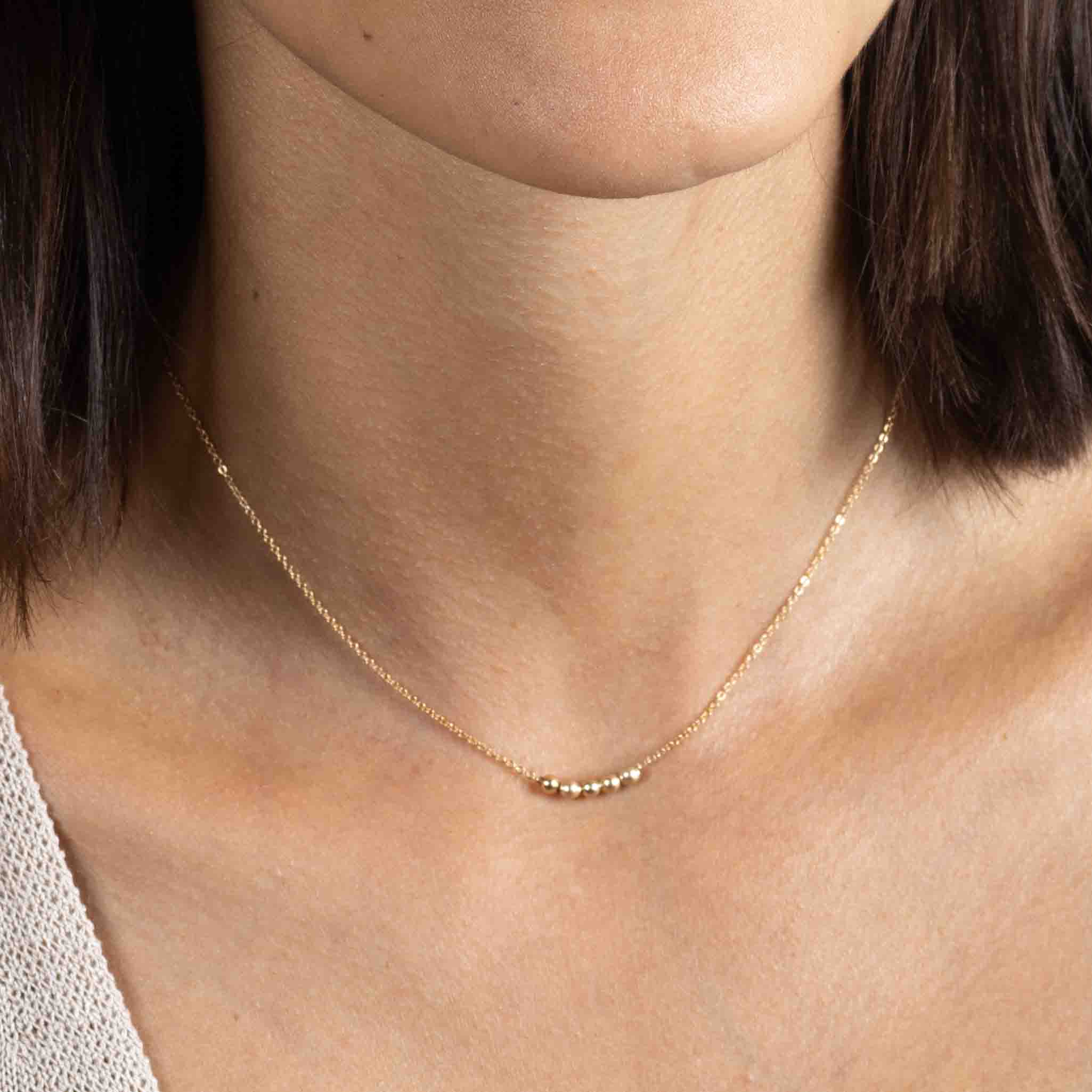 Am Hals des Models hängt eine kurze Goldkette mit fünf kleinen Goldperlen in der Mitte.