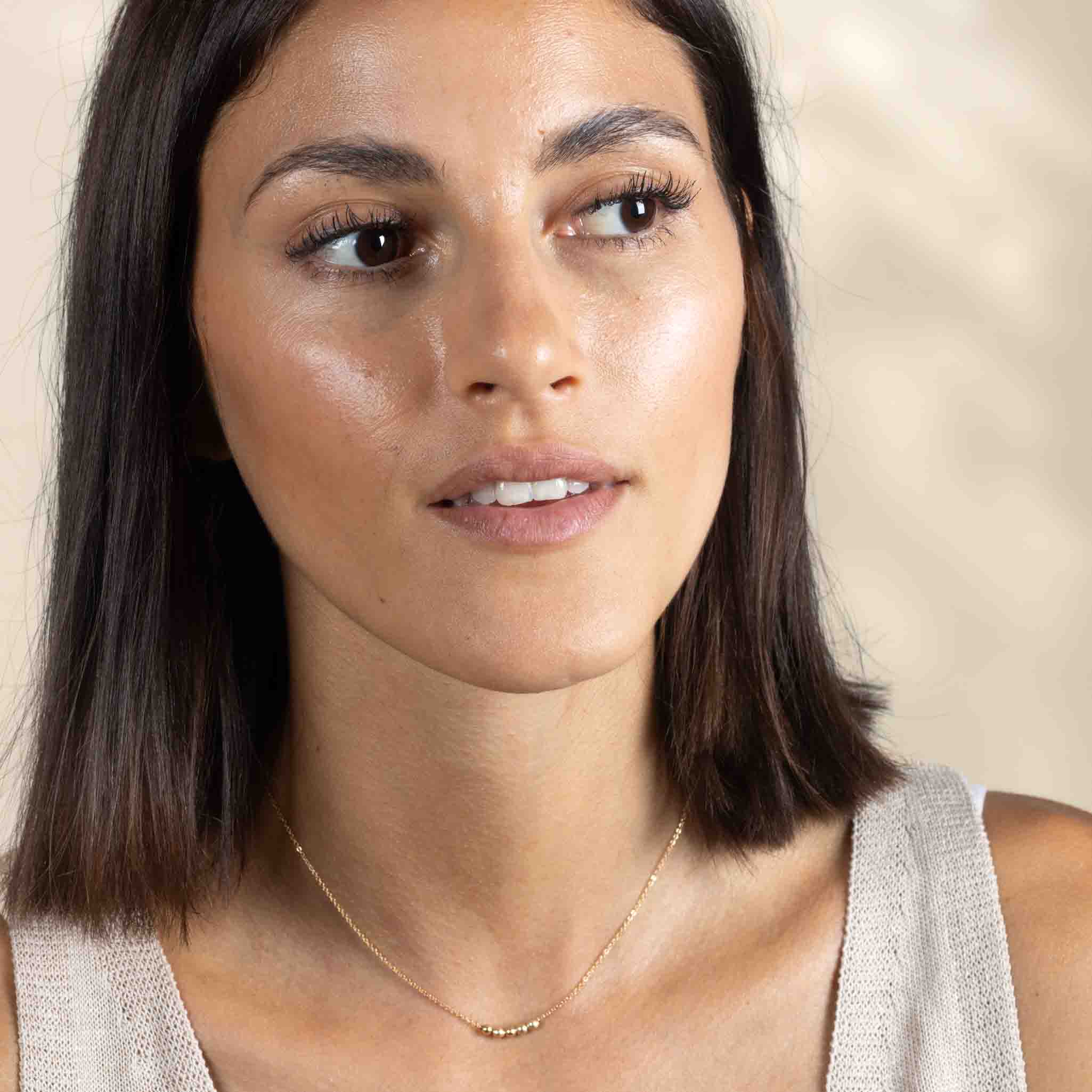 Am Hals des Models hängt eine kurze Goldkette mit fünf kleinen Goldperlen in der Mitte.