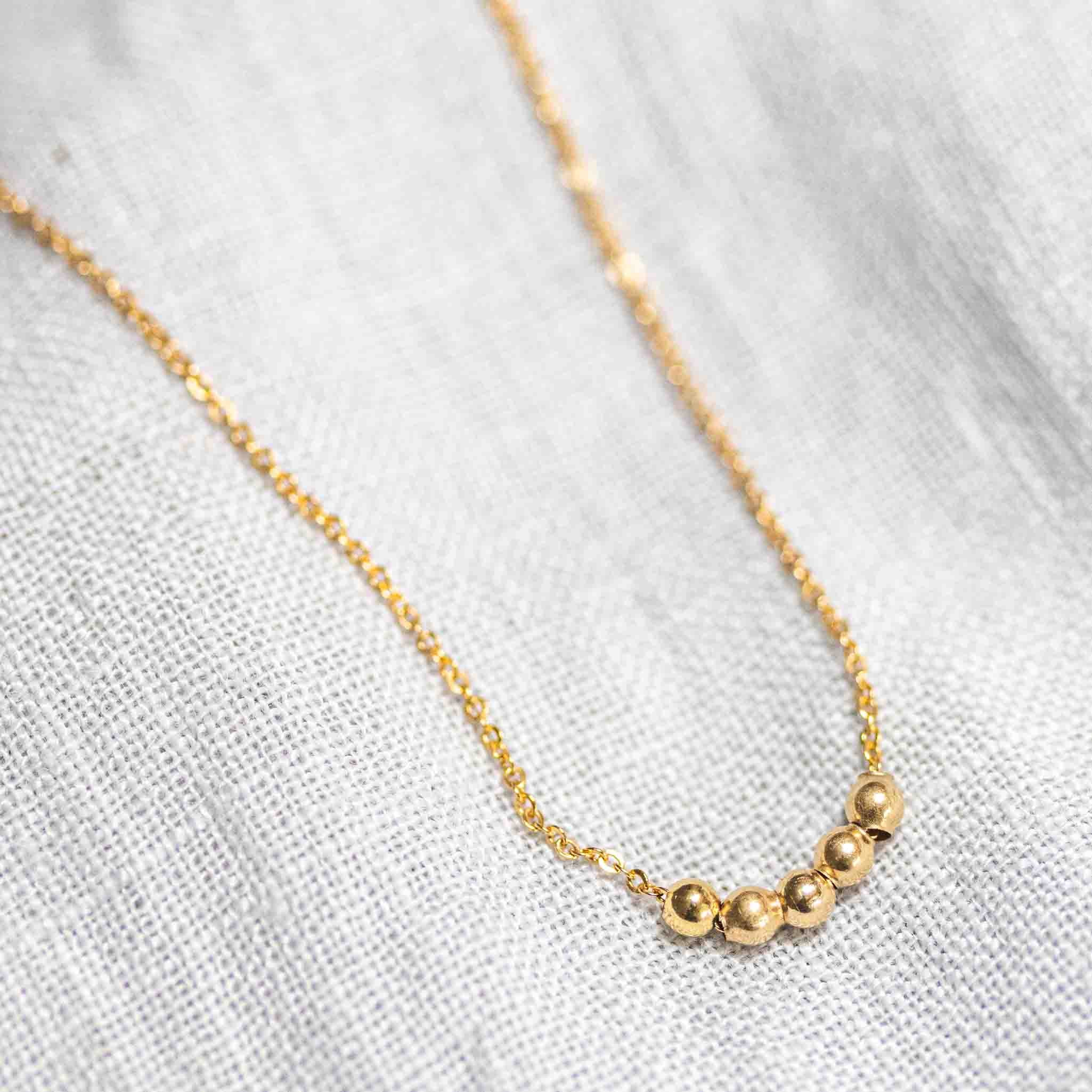 Eine feine Goldfill-Kette mit fünf kleinen Goldperlen auf weißem Hintergrund.