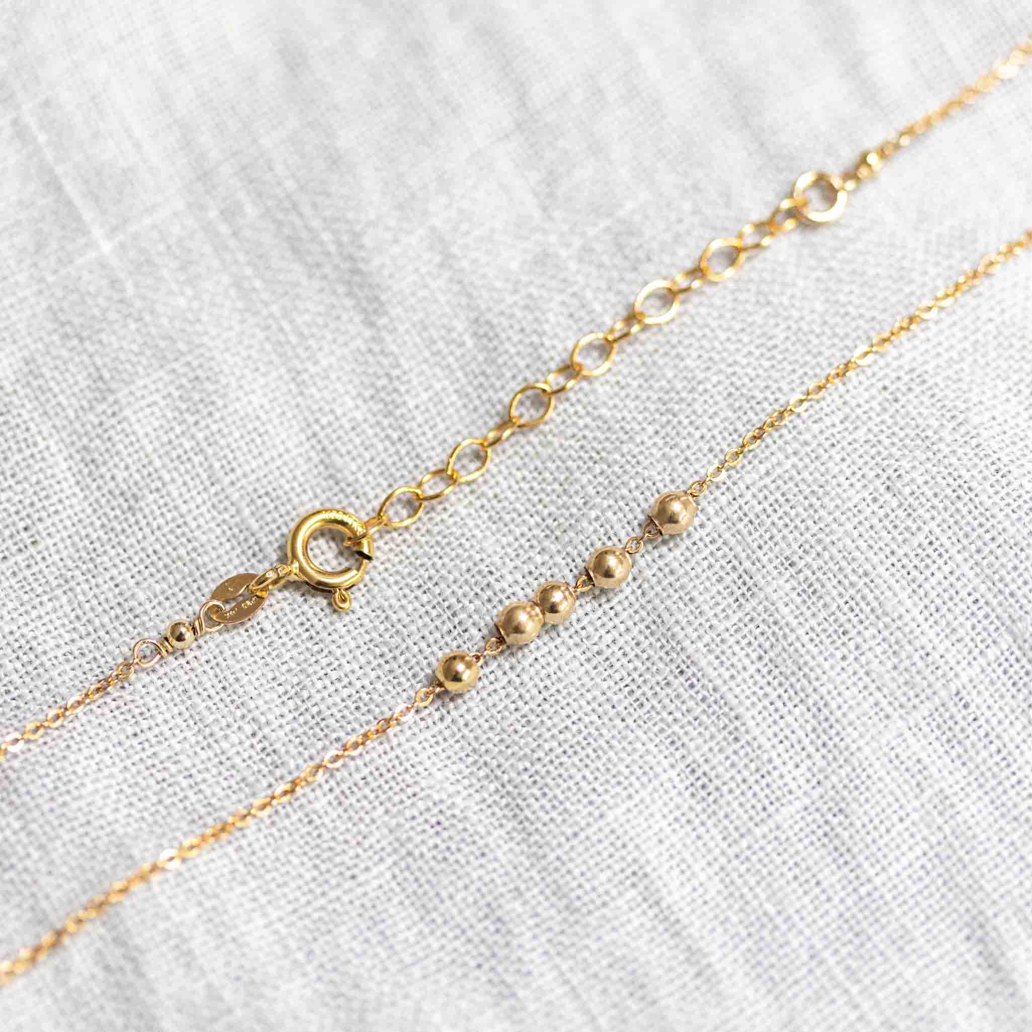 Detailansicht einer Goldkette mit fünf aufgezogenen kleinen Goldperlen und dem Verschlussbereich mit Federring und Verlängerungskettchen.