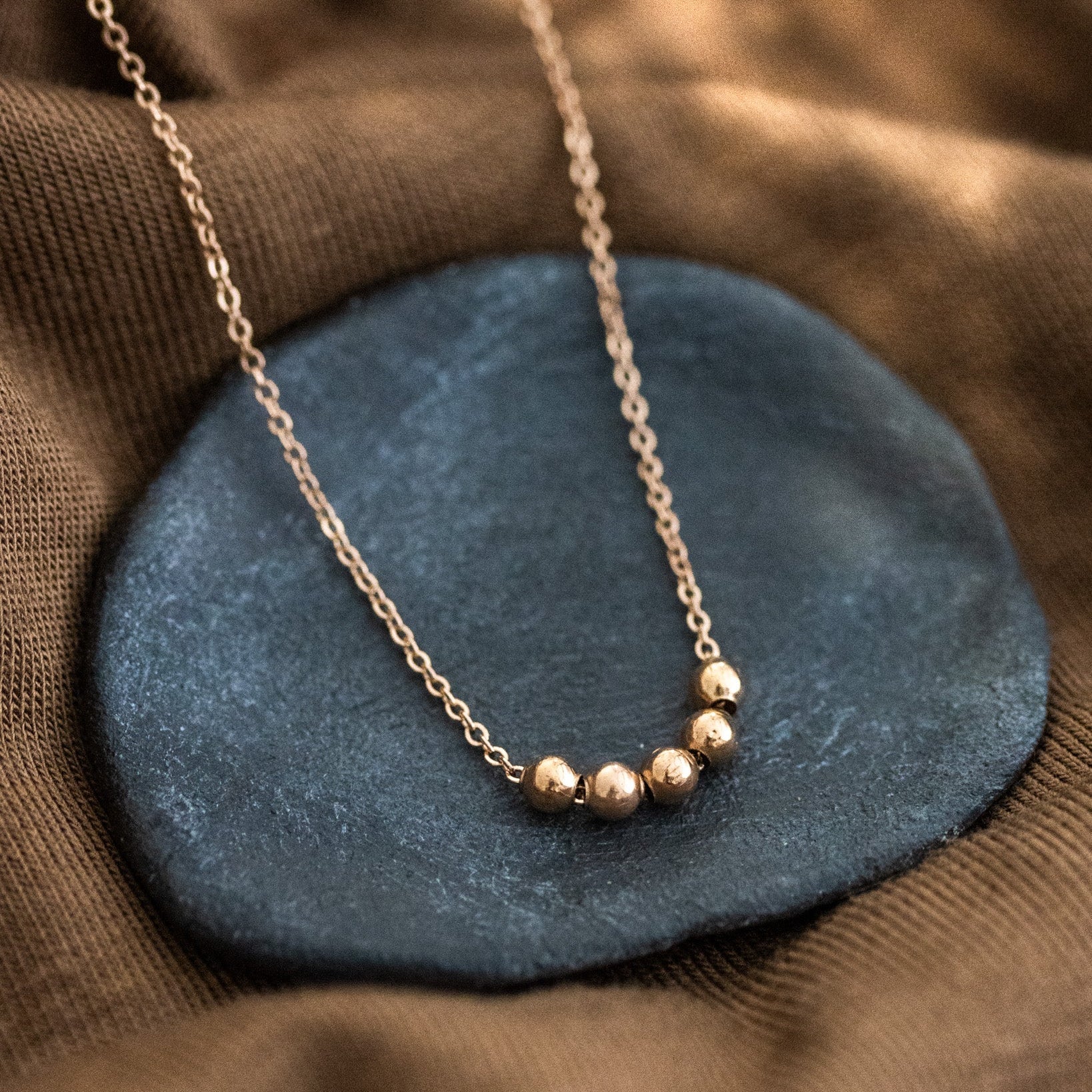 Auf einem schwarzen Schälchen liegt  eine kurze Roségold-Kette mit fünf aufgezogenen kleinen Rosegold-Perlen in der Mitte.