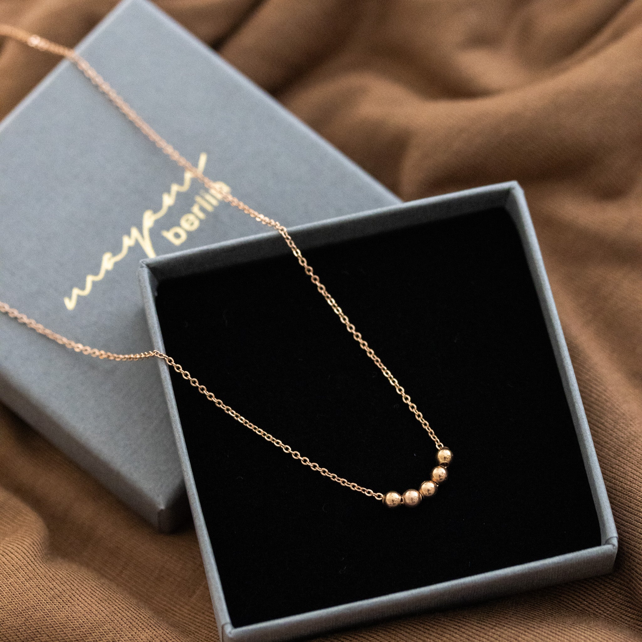 Im offenen Schmucketui liegt eine kurze Roségold-Kette mit fünf aufgezogenen kleinen Rosegold-Perlen in der Mitte.