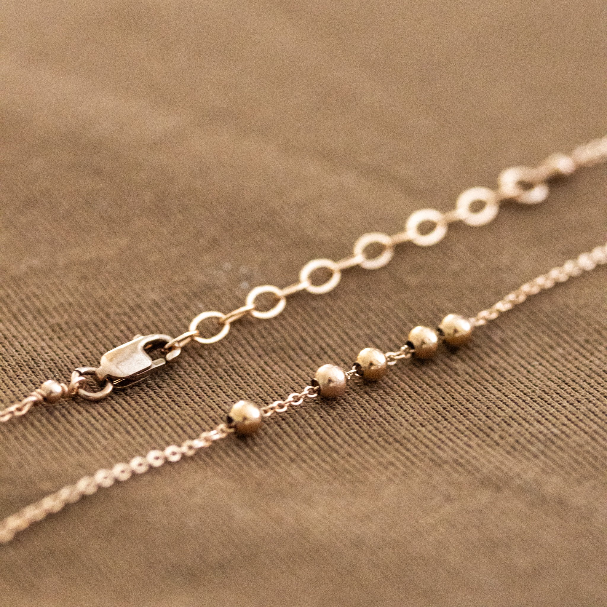 Detail-Aufnahme einer feinen Roségold-Kette mit Karabinerverschluss, Verlängerungskettchen und fünf kleinen Metallperlen.