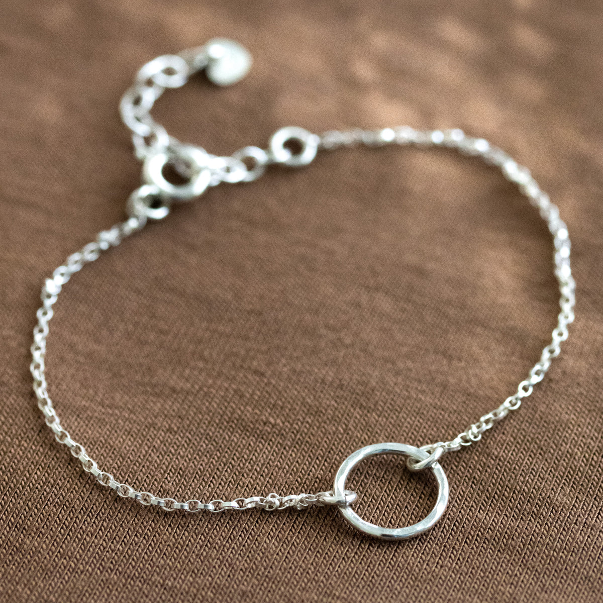 925 Sterlingsilber Armband mit gehämmerten Kreis-Anhänger in der Mitte auf braunem Untergrund ausgelegt.