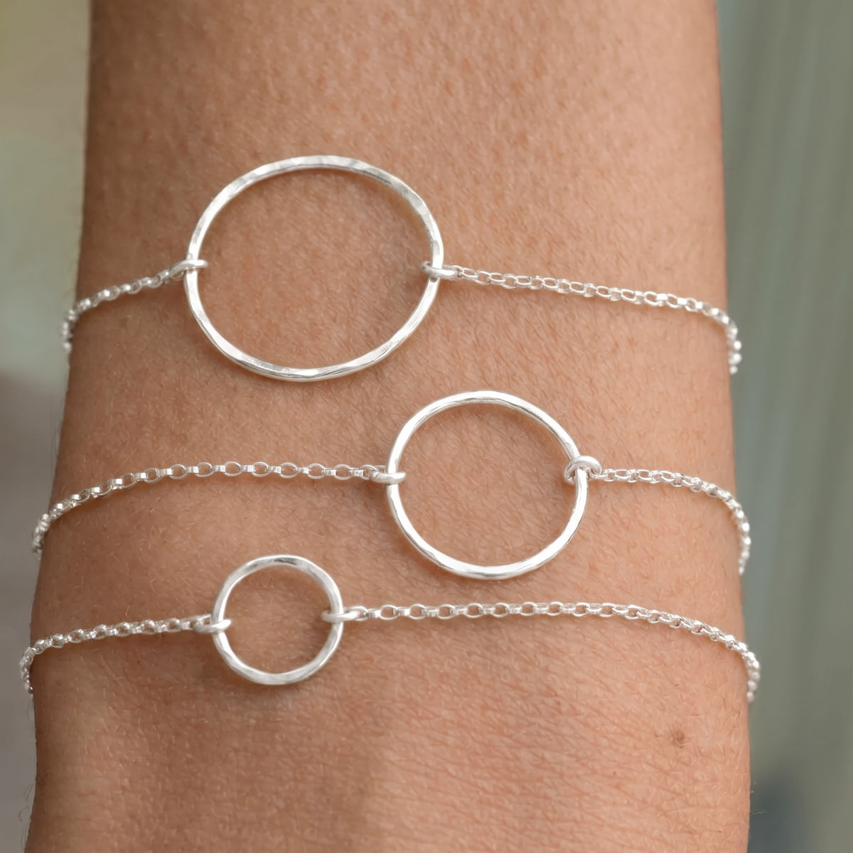 Drei zarte Armbänder aus Sterlingsilber mit gehämmerten Kreisanhängern in drei Größen, übereinander am Handgelenk getragen.