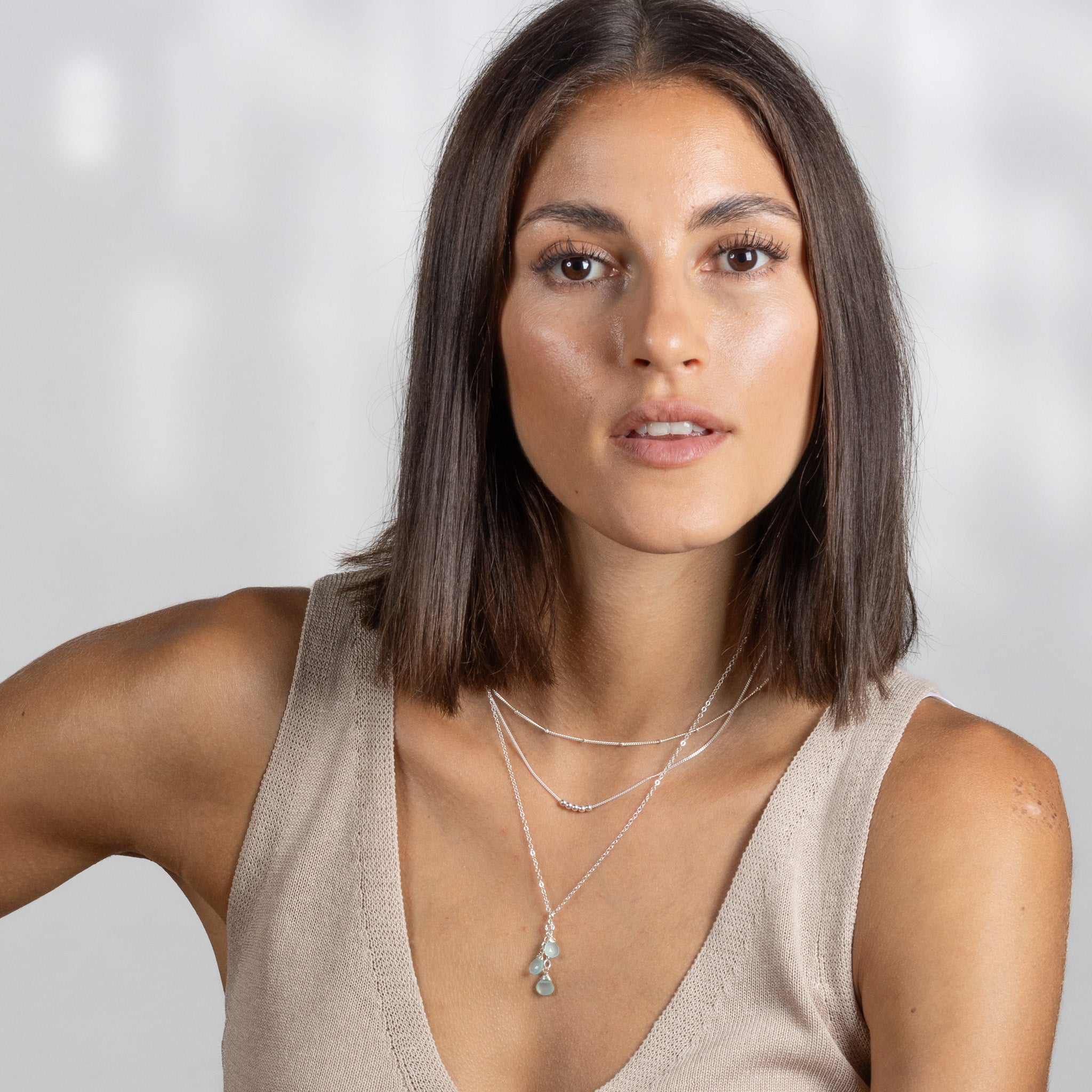 Am Hals des Models sind drei unterschiedlich lange Silberketten angebracht. An der untersten hängen drei hellblaue Edelsteine.