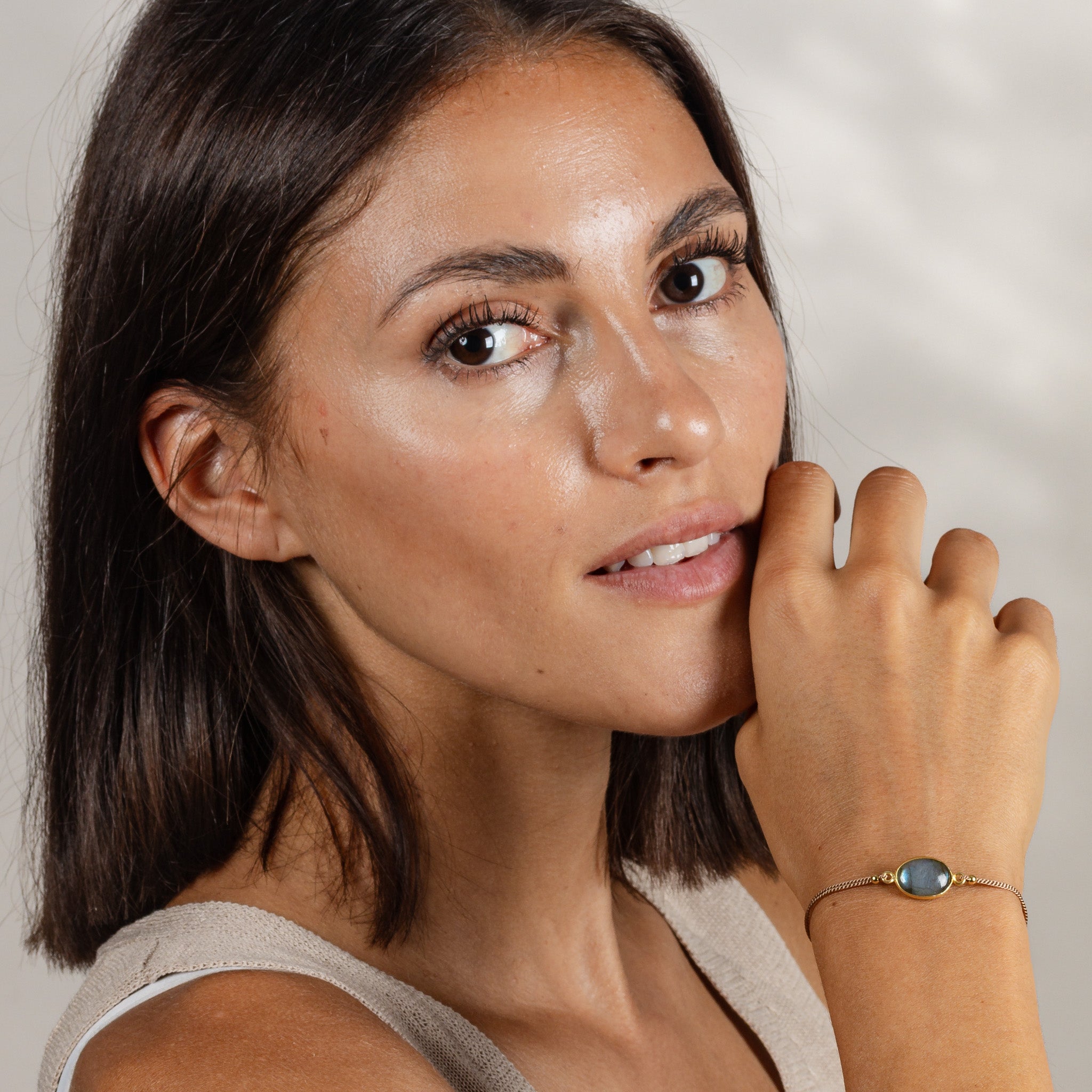 Das Model trägt ein dünnes Seidenarmband mit einem ovalen Labradorit Edelstein in der Mitte.