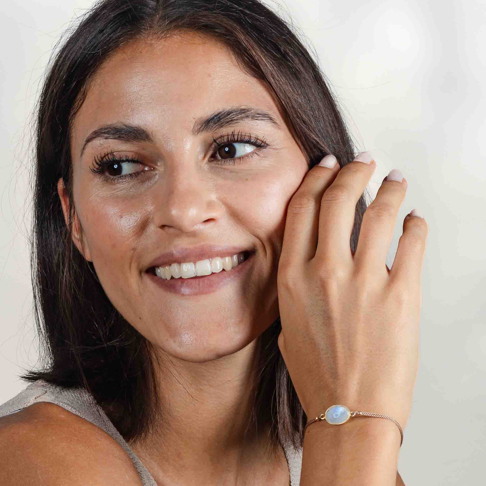 Das Model trägt ein feines Seidenarmband mit einem ovalen und gold gefassten Mondstein in der Mitte an ihrem Handgelenk.