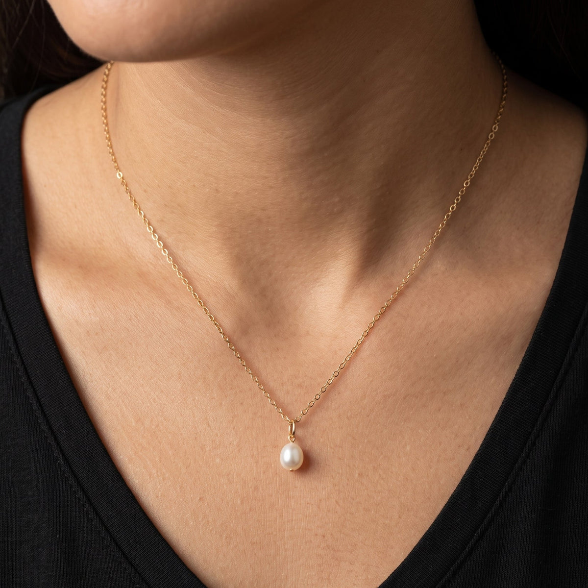 Eine feine Goldkette mit einem ovalem Perlenanhänger am Hals getragen.
