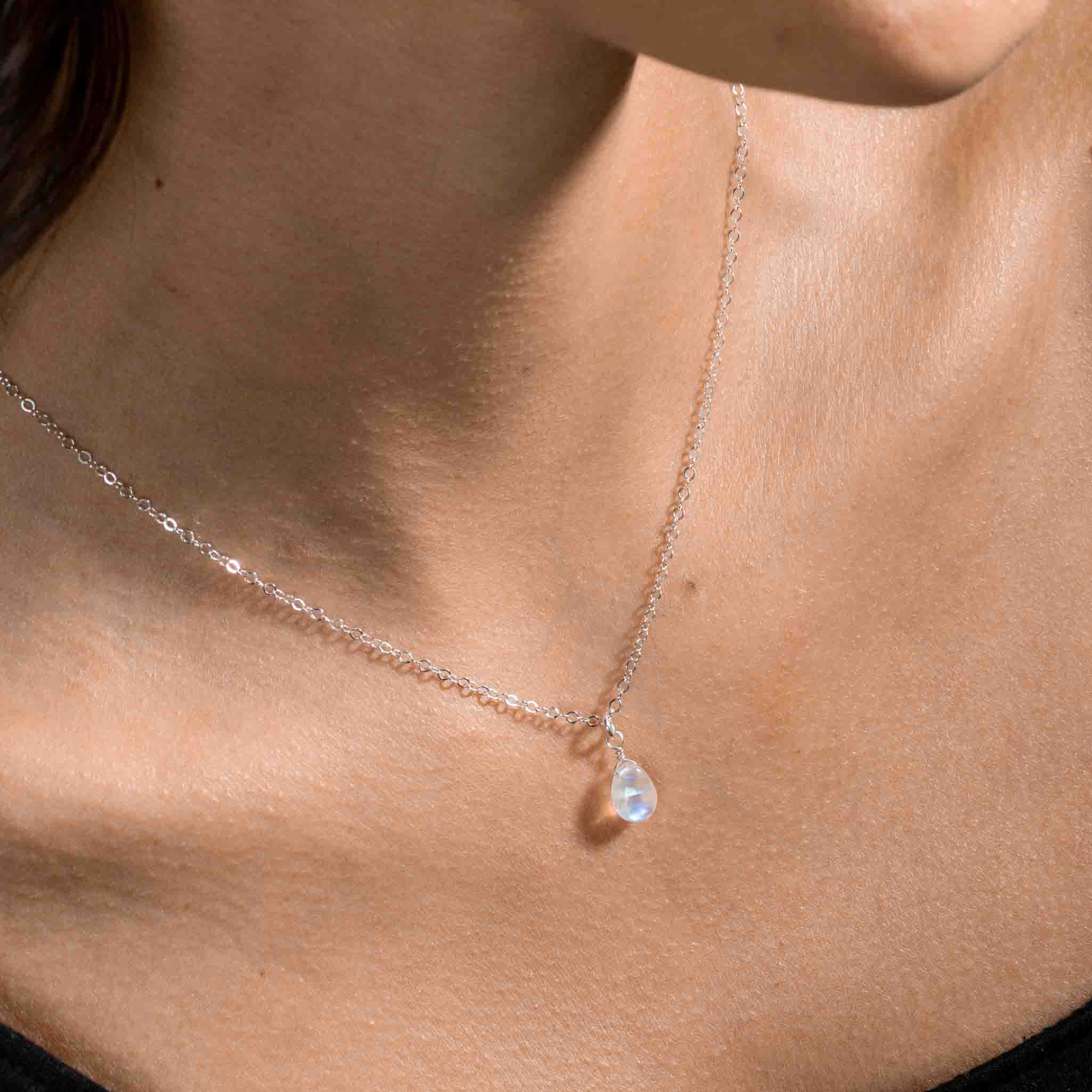Eine feine Silberkette mit einem kleinen, bläulich schimmernden Mondstein-Anhänger in Tropfenform hängt am Hals des Models.