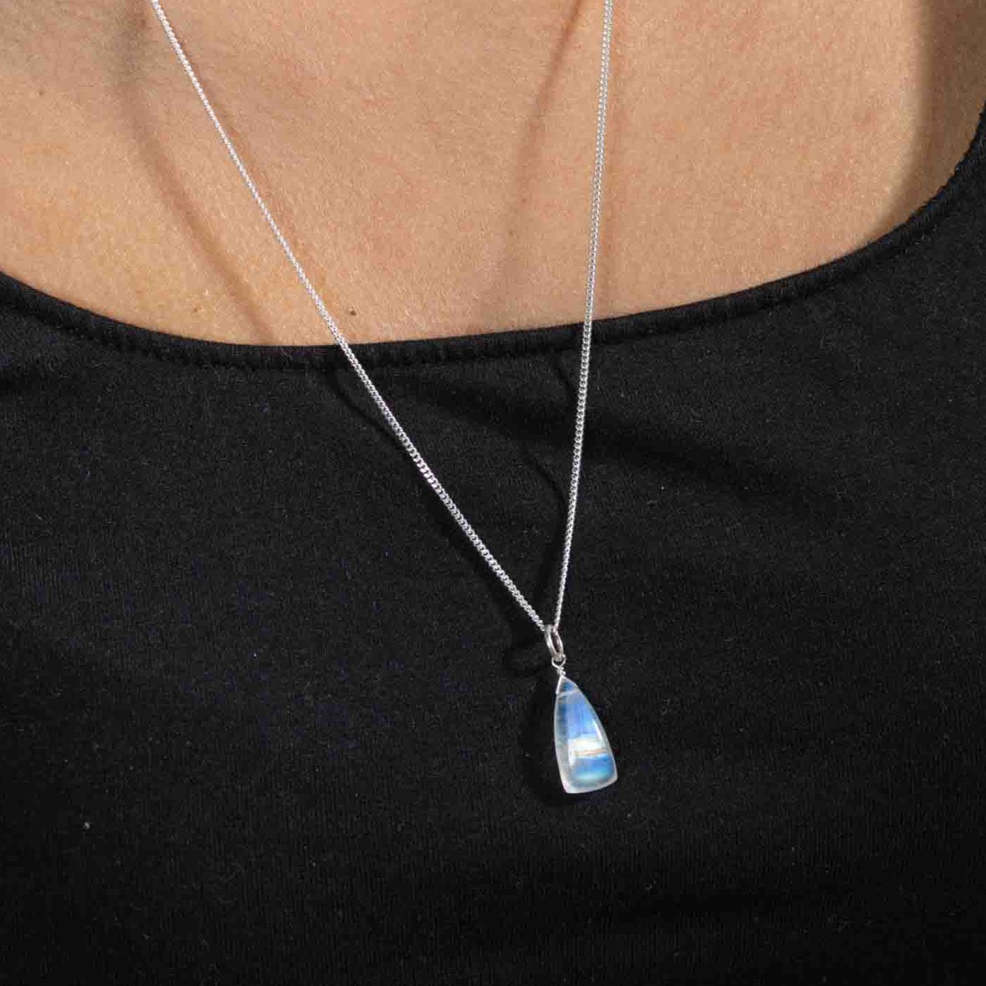 Am Hals des Models hängt eine lange Silberkette mit einem Mondstein-Anhänger. Der Stein hat die Form eines länglichen Dreiecks und schimmert bläulich, gelb und orange.