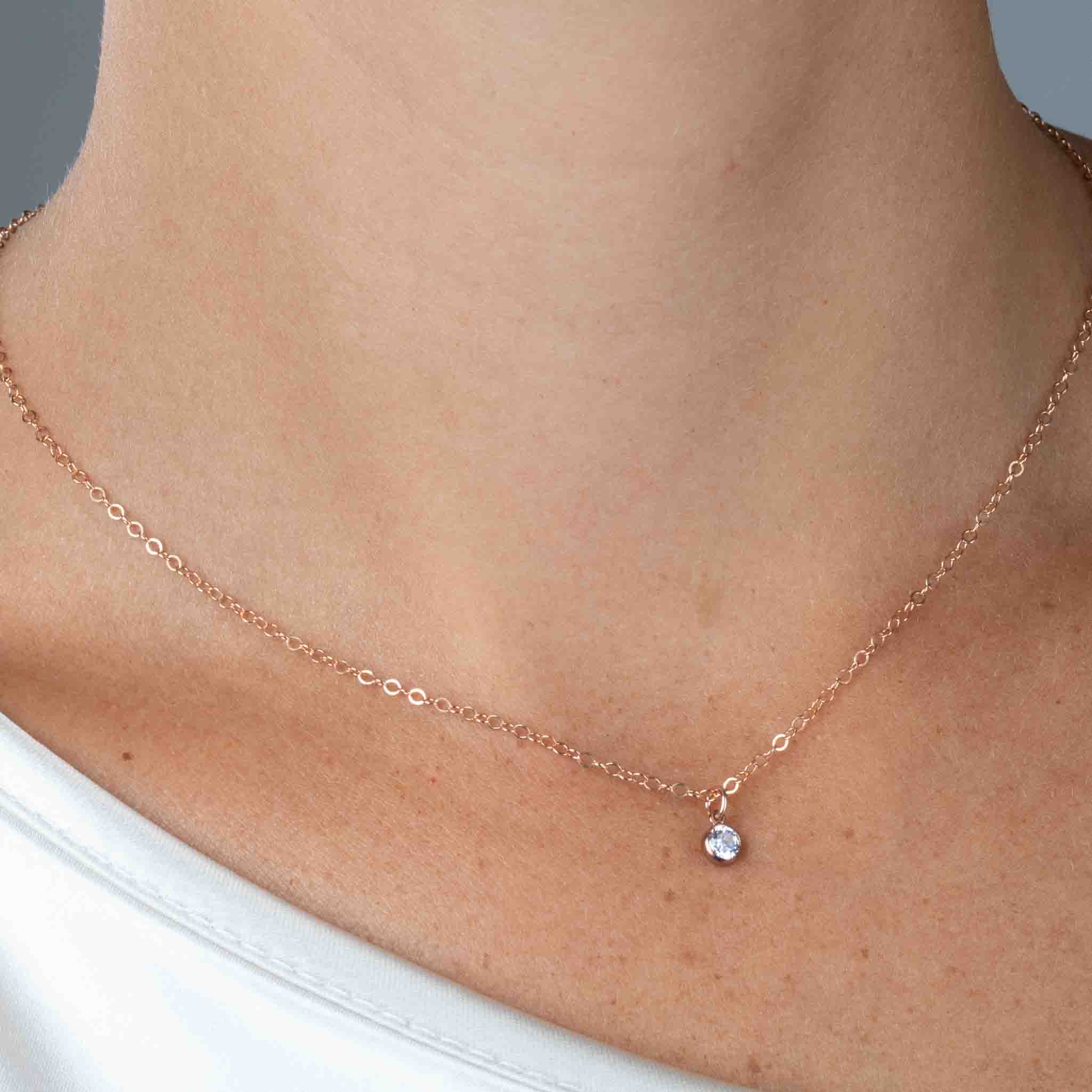 Nahaufnahme einer feinen, rose goldenen Kette mit winzigem, runden Zirkonia-Anhänger am Hals des Models