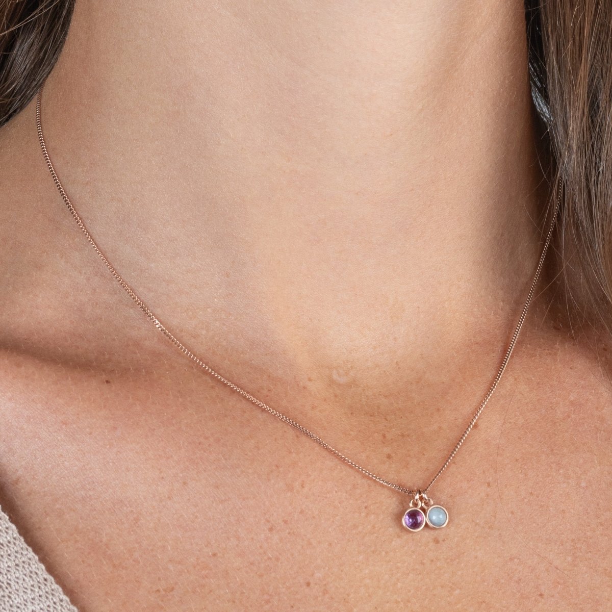 Am Hals des Models hängt eine rosé goldene Kette mit zwei winzigen, runden Anhängern, einem Amethyst und einem Aquamarin.