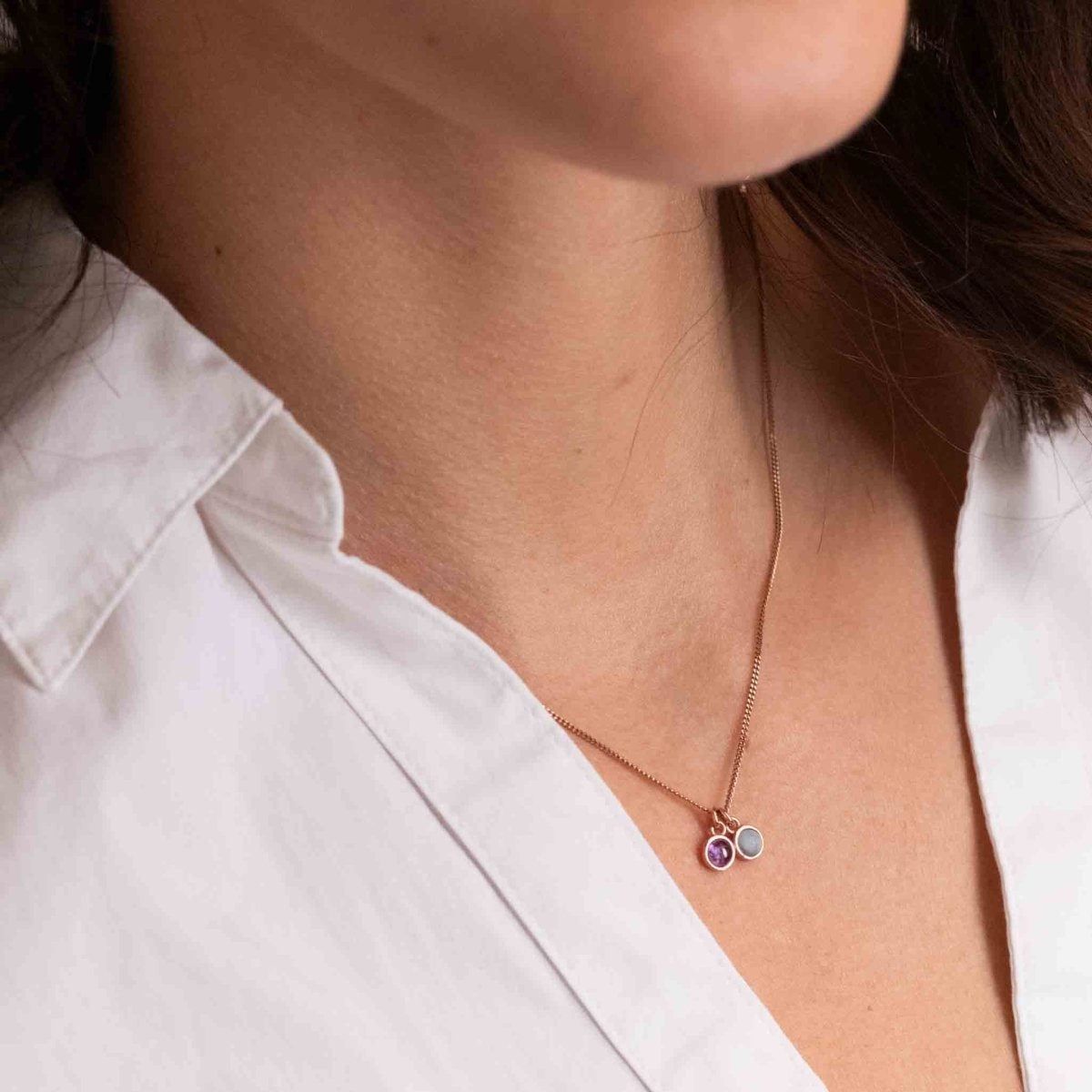 Am Hals des Models hängt eine rosé goldene Kette mit zwei winzigen, runden Anhängern, einem Amethyst und einem Aquamarin.