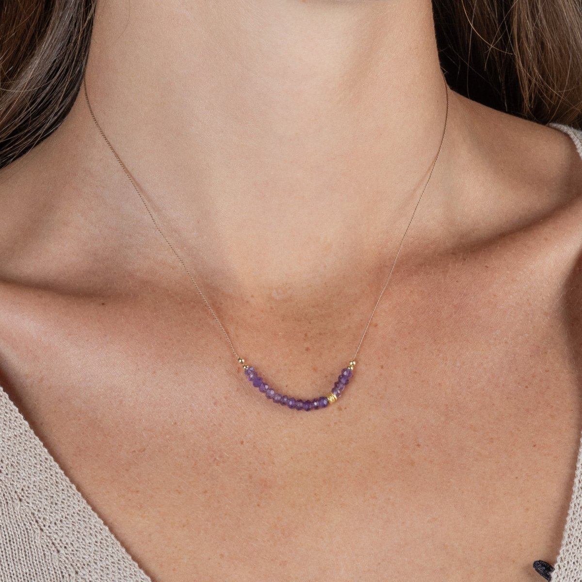 Am Hals des Models hängt eine dünne Seidenkette mit einer Reihe violetter Amethyst-Rondellen und goldenen Zierperlen in der Mitte.
