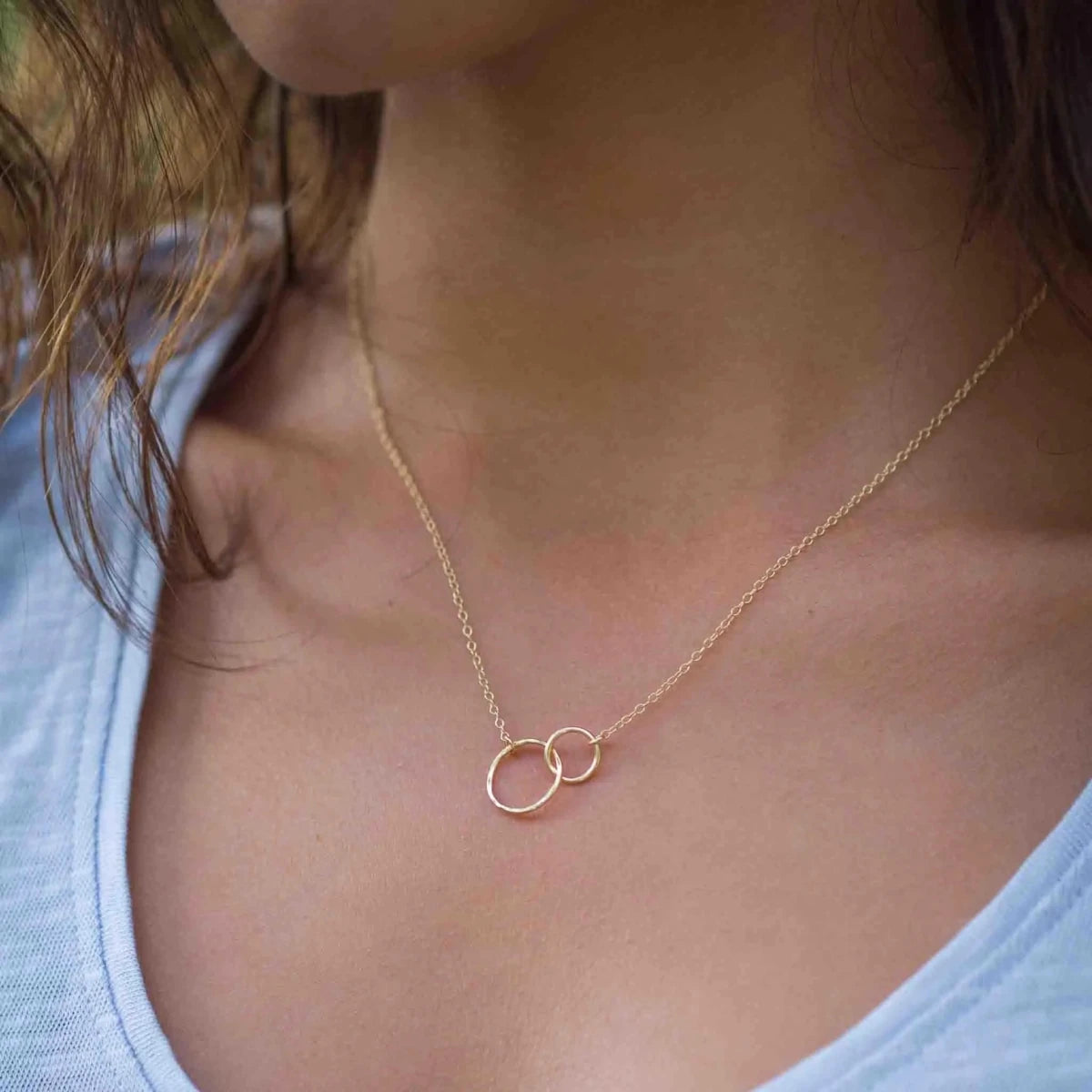 Am Hals des Models hängt eine feine Goldkette mit zwei unterschiedlich großen, ineinander verschlungenen Ringen in der Mitte.