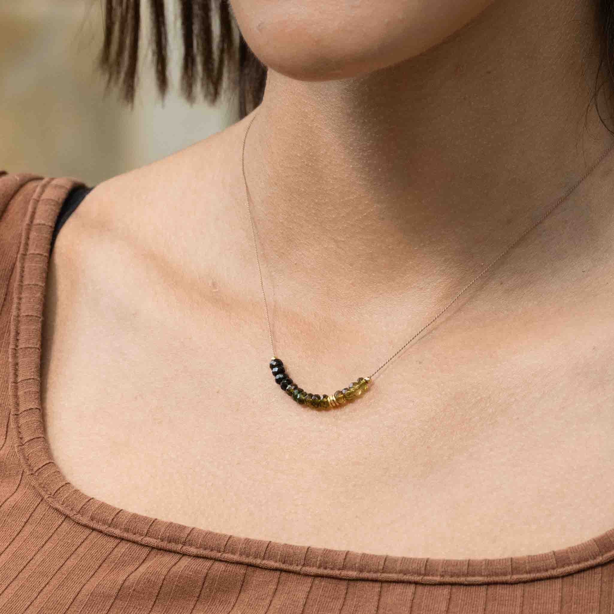 Am Hals des Models hängt eine dünne Seidenkette mit einer Reihe grüner Turmalin-Rondellen und goldener Zierperlen in der Mitte.