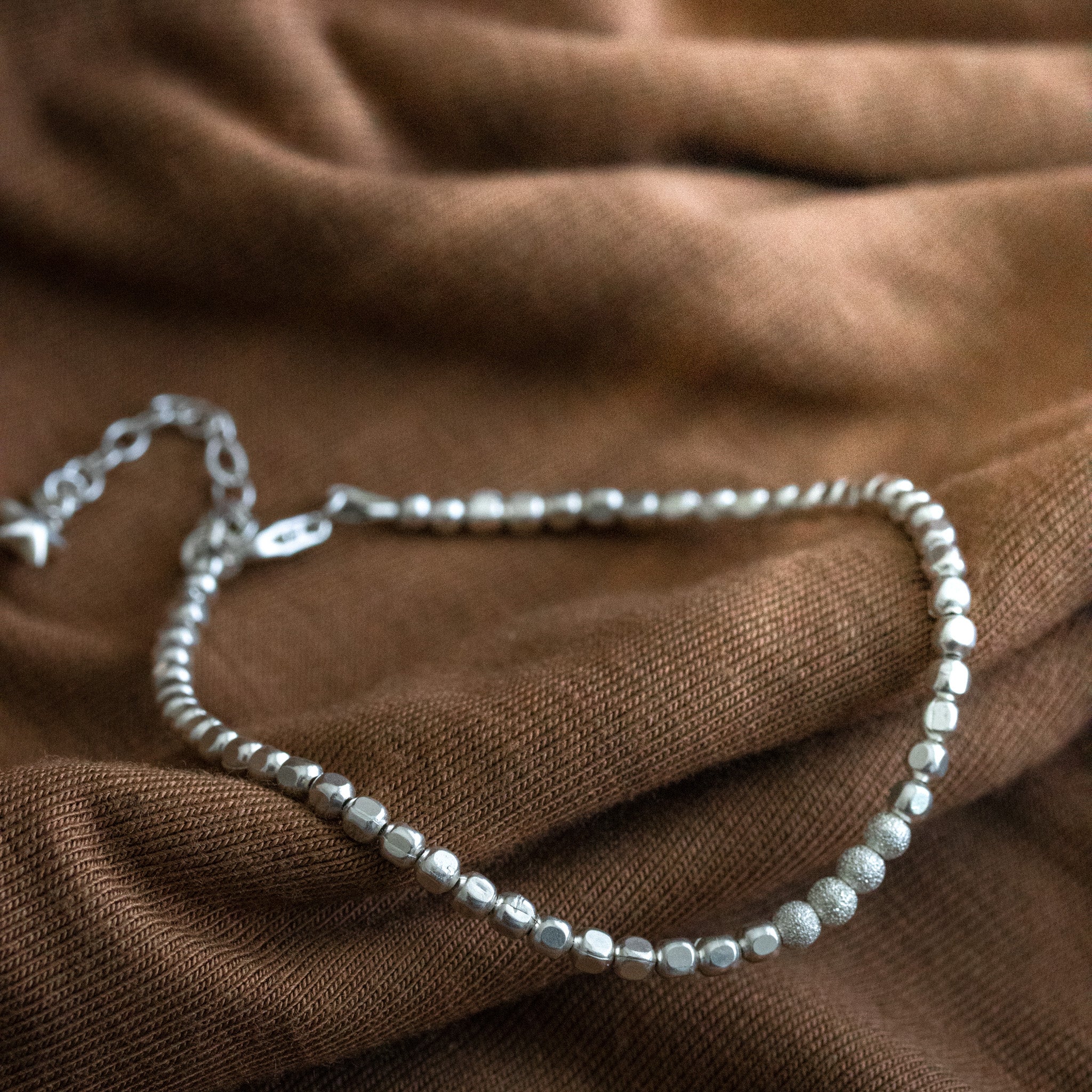 925 Silber Würfel-Armband mit gefrosteten Perlen in der Mitte auf braunem Stoff ausgelegt.