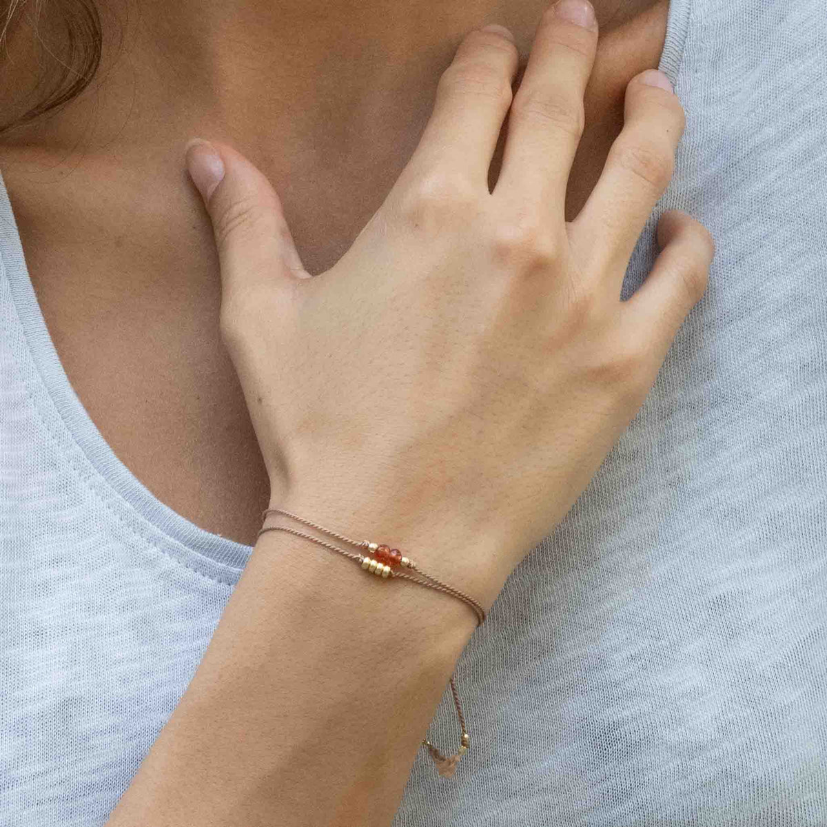 Zwei unterschiedliche dünne, braune Schnurarmbänder mit Karneol und goldenen Perlen am Handgelenk getragen.