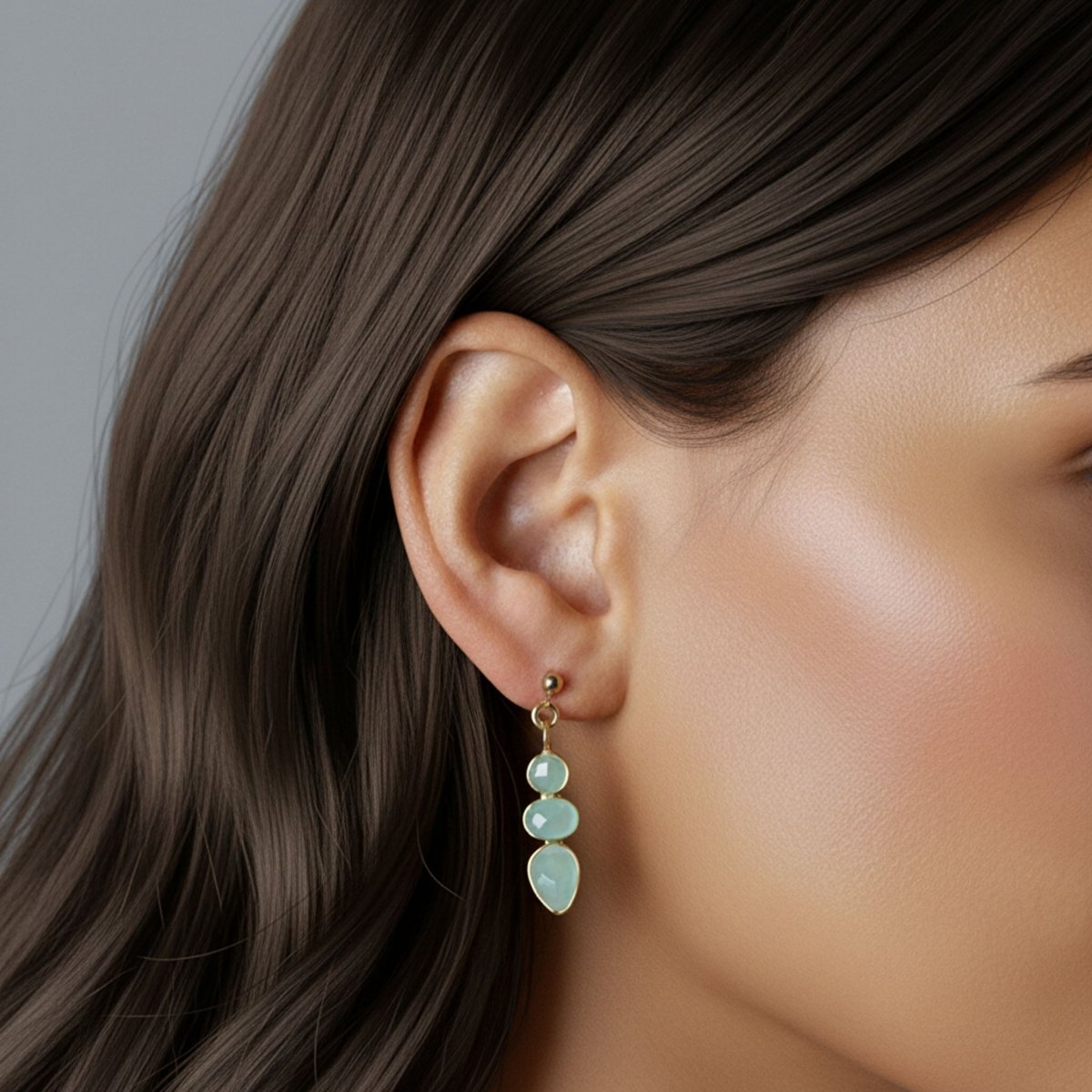 Am Ohr des Models hängt ein goldener Ohrstecker mit drei Aqua Chalcedonen.