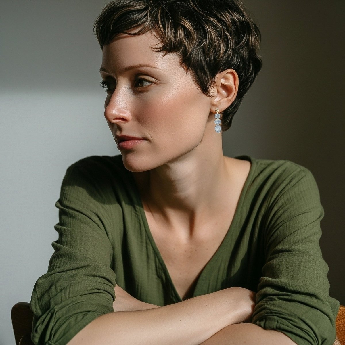 Ein goldener Ohrstecker mit einem dreifachen Mondstein-Anhänger hängt am Ohr des Models.