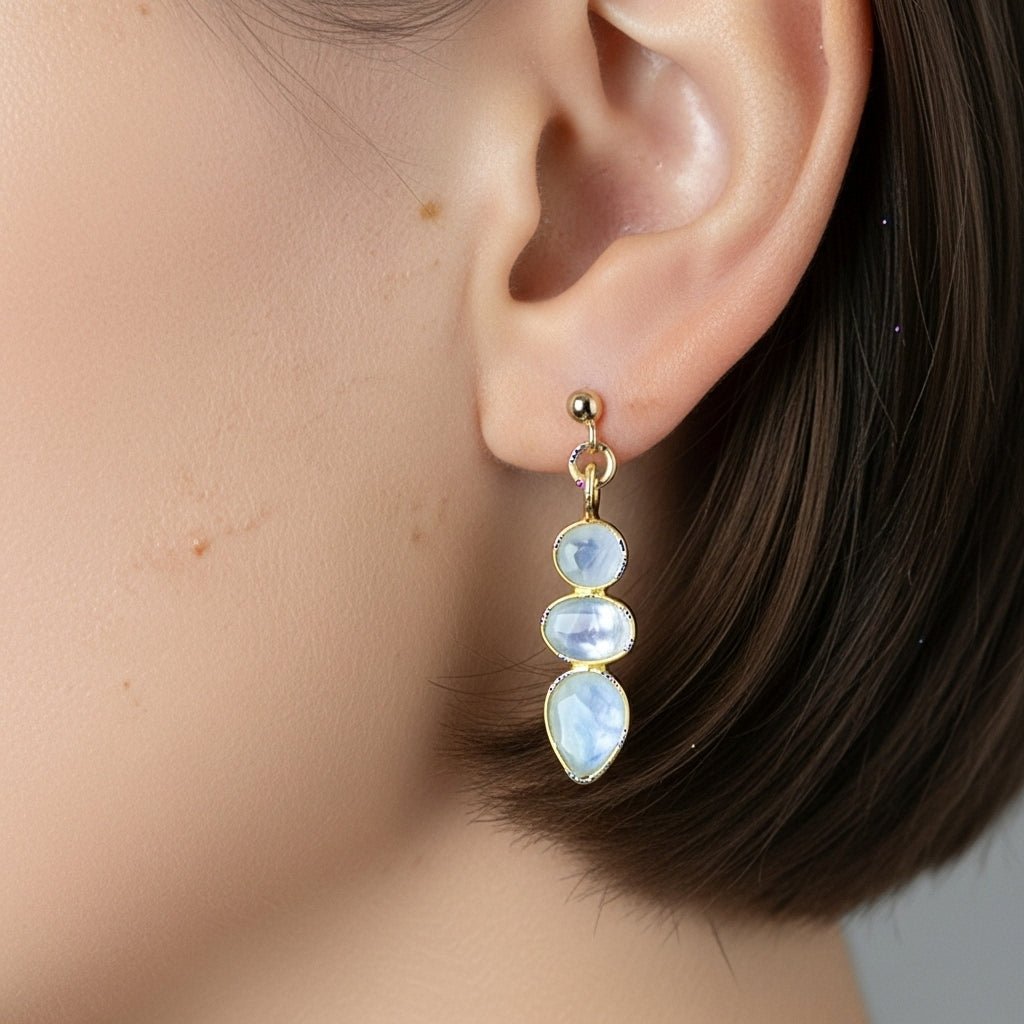 Ein goldener Ohrstecker mit einem dreifachen Mondstein-Anhänger hängt am Ohr des Models.