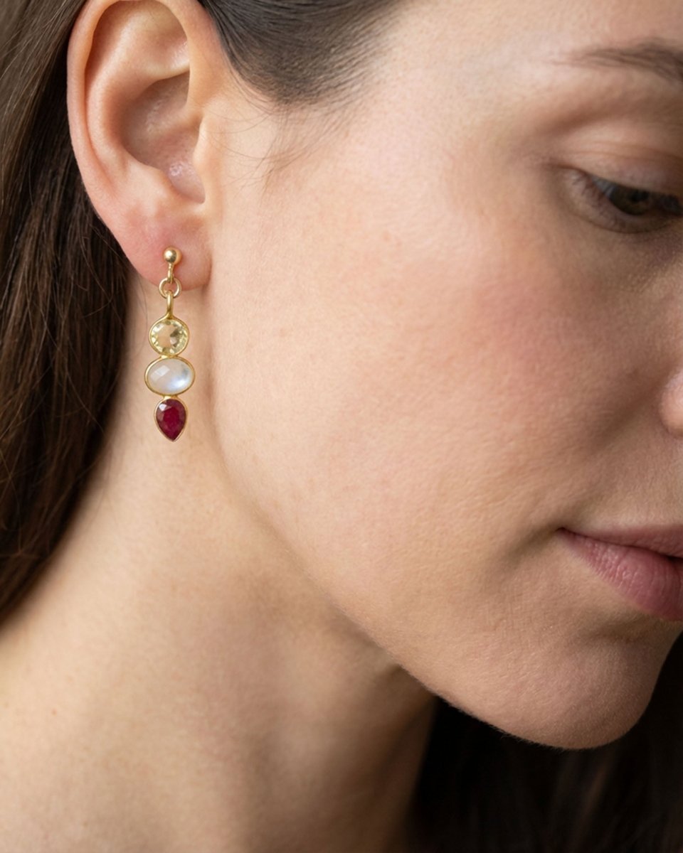 Am Ohr des Models hängt ein länglicher Ohrstecker mit drei gold gefassten Edelsteinen: Citrin, Mondstein und Rubin. Die Steine sind untereinander angebracht.