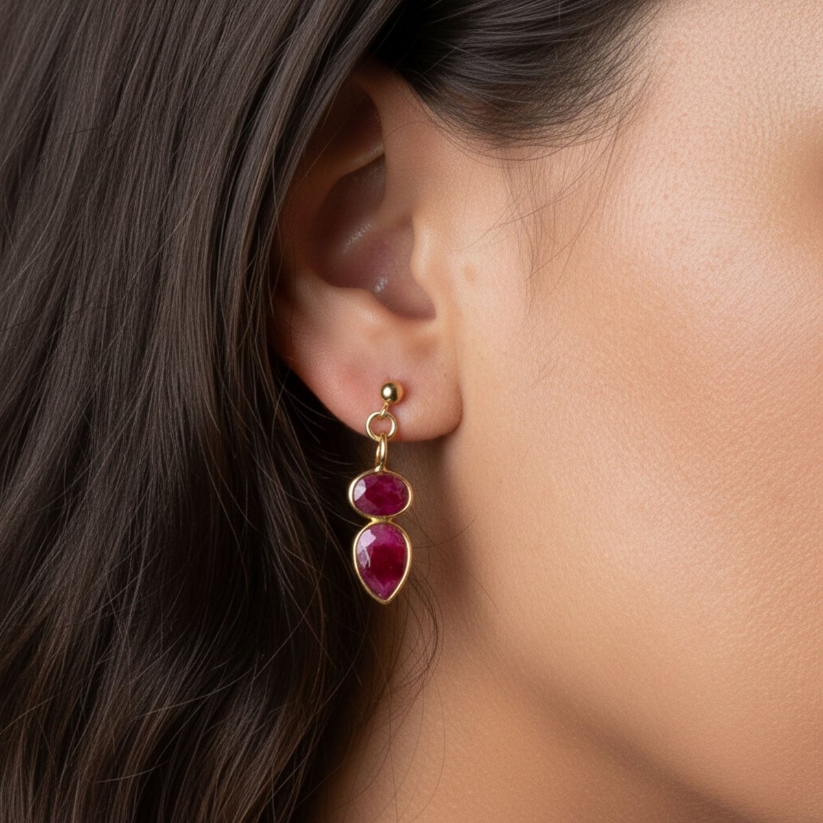 Ein goldener Ohrstecker mit zwei übereinander angebrachten Rubinen hängt am Ohr des Models.