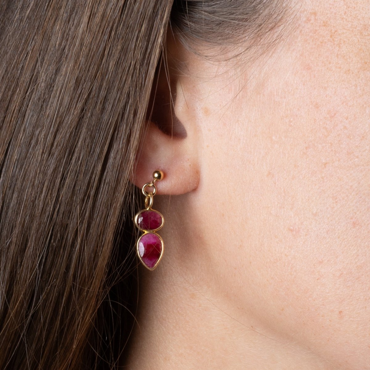 Ein goldener Ohrstecker mit zwei übereinander angebrachten Rubinen hängt am Ohr des Models.