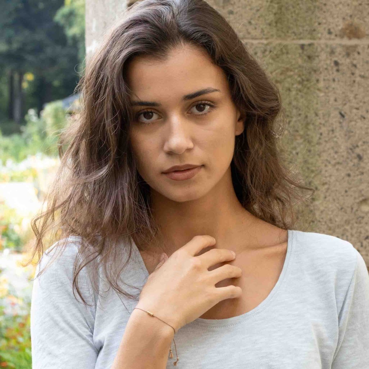 Am Handgelenk des Models ist ein feines Armband zu sehen. Es besteht aus einer beigen Seidenschnur mit vier goldenen Perlen in der Mitte.