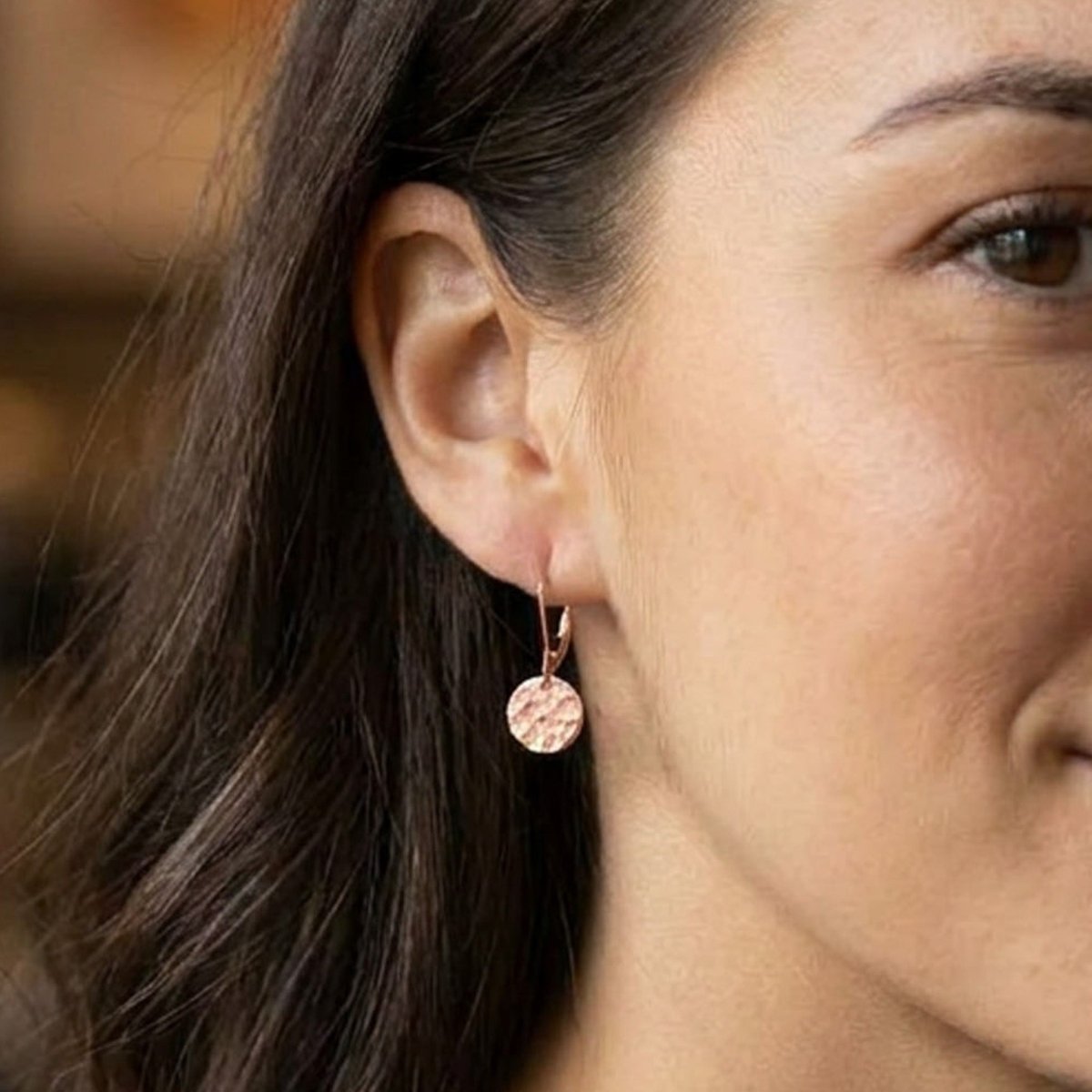 Am Ohr des Models hängt ein rosé goldener Ohrring mit einem gehämmerten, runden Plättchen.