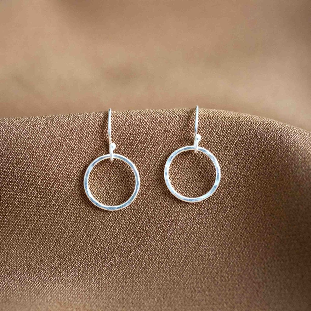 Ein Paar simpler 925 Silber Ohrringe mit offenem Kreis auf beigem Hintergrund.