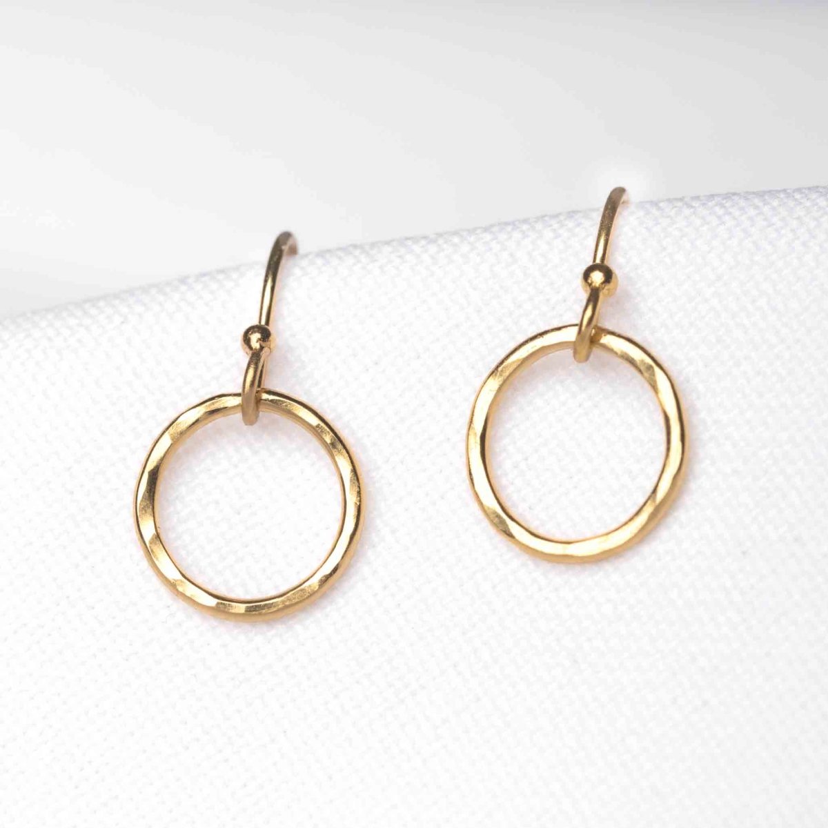 Ein Paar goldener Ohrringe von Mayam Berlin mit Ohrhaken, an denen jeweils ein offener Ring hängt, auf weißem Hintergrund