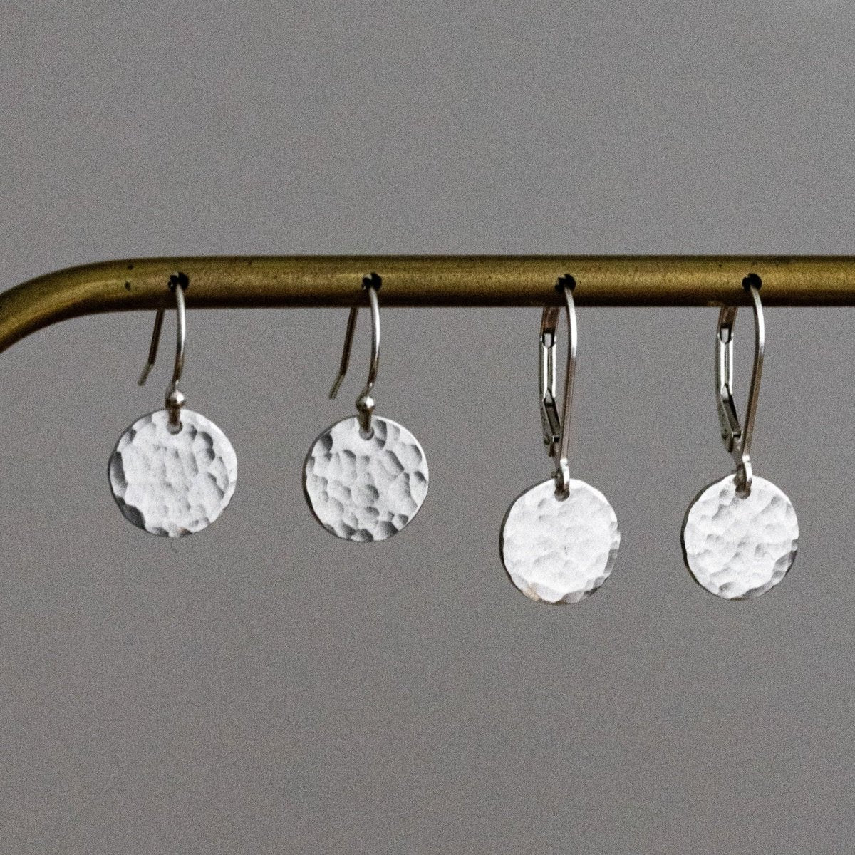 Zwei Paar 925 Silber-Ohrringe mit gehämmerten Plättchen hängen an einer Kupferstange.