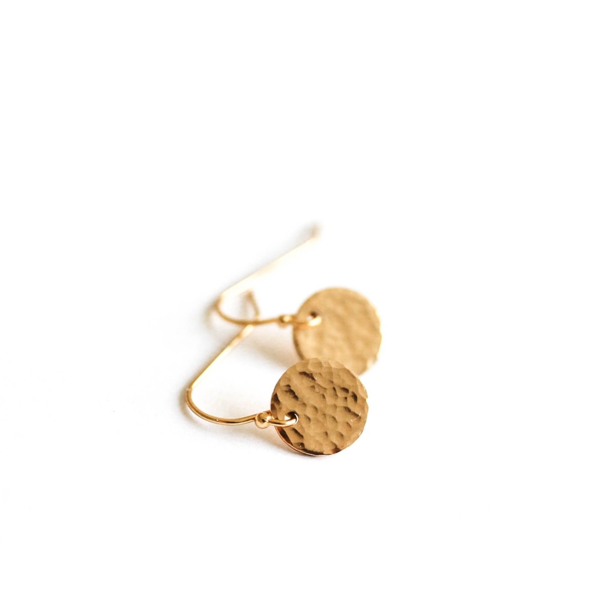 Ein Paar goldener Ohrringe auf weißem Hintergrund. Die Ohrringe bestehen aus einfachen Ohrhaken, an denen jeweils ein rundes, gehämmertes Plättchen hängt.