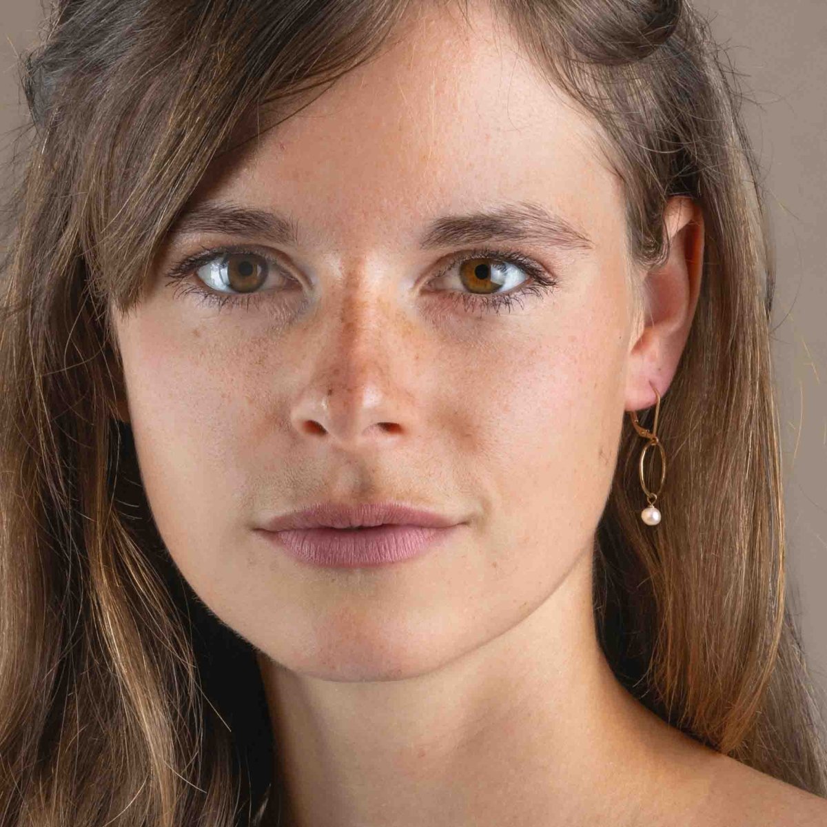 Ein goldener Ohrring mit einem gehämmerten, offenen Ring und einer kleinen, weißen Perle am Ohr des Models