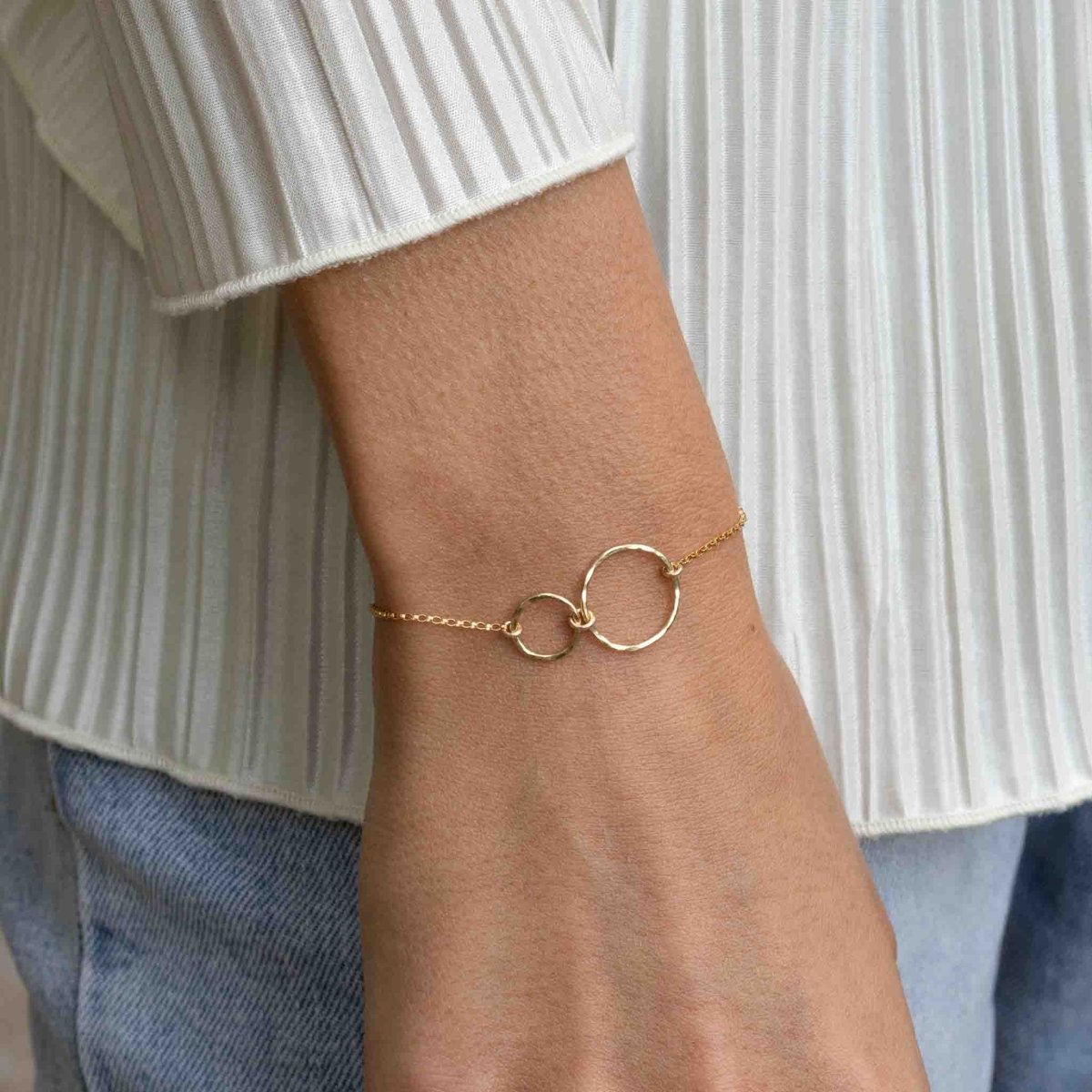 Ein dünnes Goldarmband mit zwei leicht gehämmerten, offenen Ringen am Handgelenk des Models.