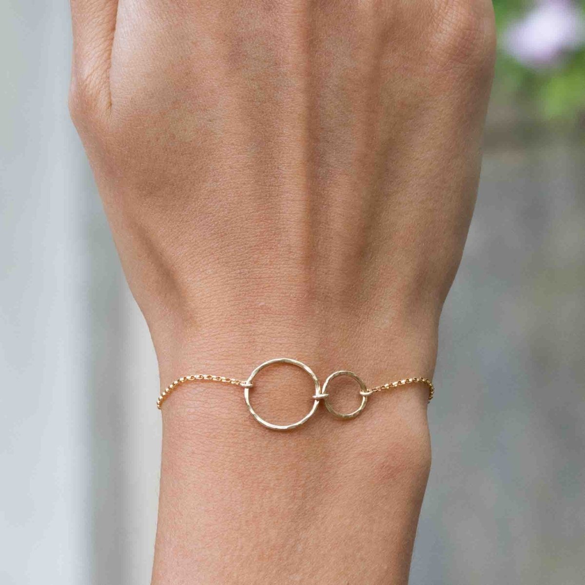 Ein dünnes Goldarmband mit zwei leicht gehämmerten, offenen Ringen am Handgelenk des Models.