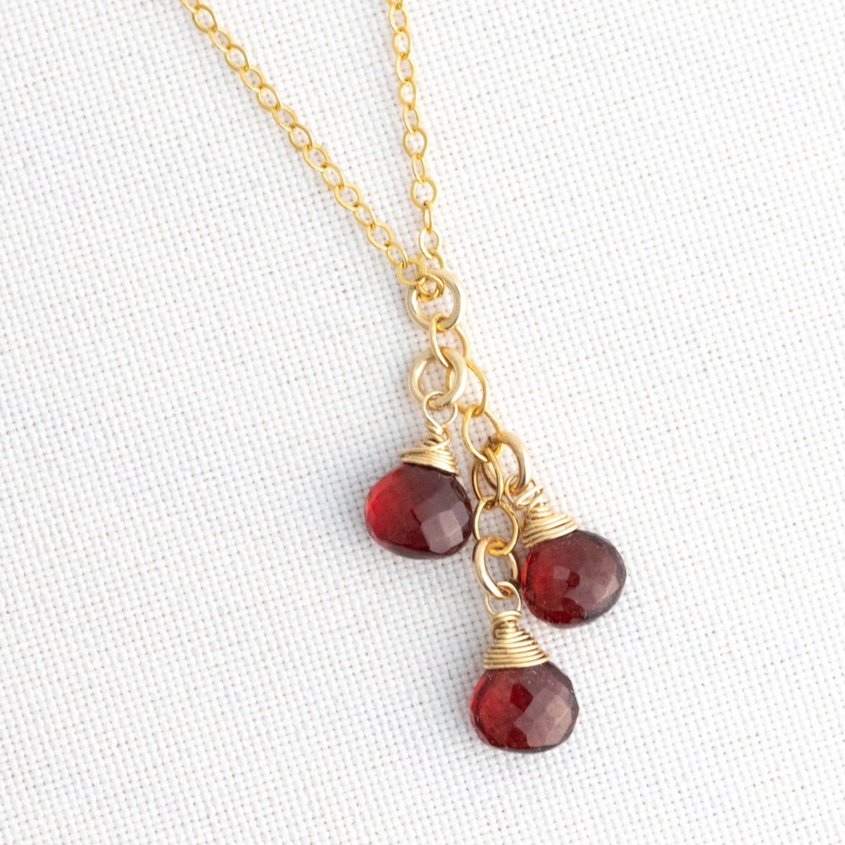 Eine feine Goldkette mit drei untereinander hängenden Granat Edelsteinen hängt vor weißem Hintergrund.