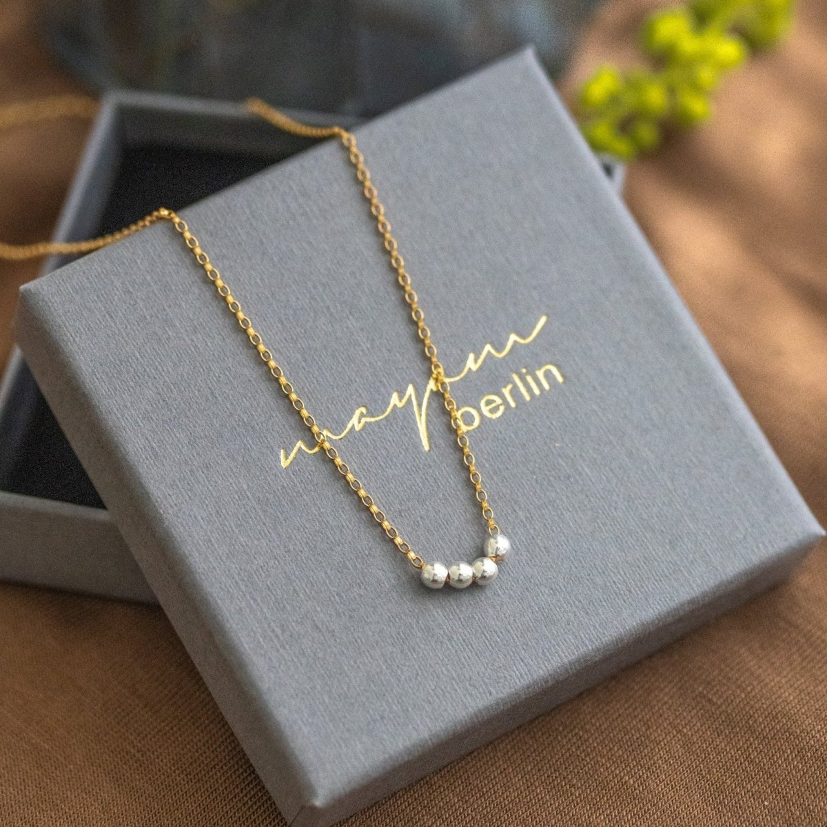 Eine Goldkette mit einer Reihe kleiner Silberperlen in der Mitte liegt auf einem grauen Schmucketui mit der Beschriftung "mayam berlin".