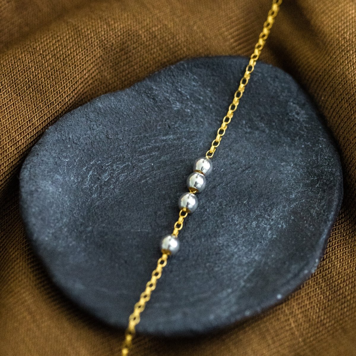 Eine Goldkette mit einer Reihe kleiner Silberperlen in der Mitte liegt auf einem schwarzen Schälchen.