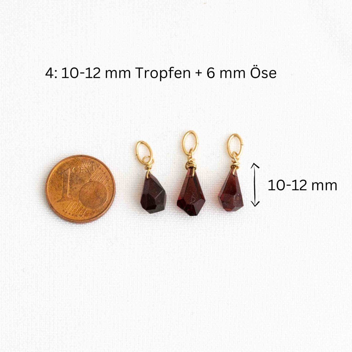 Drei unregelmäßig facettierte Granat Kettenanhänger neben einer 1-Cent-Münze auf weißem Hintergrund.